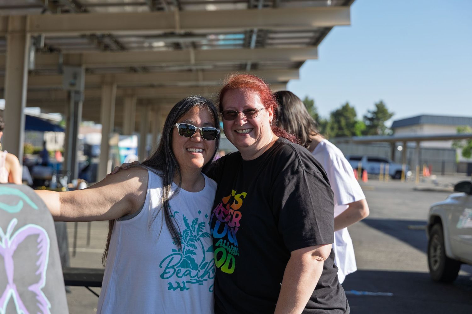 A happy group wearing sunglasses and casual attire poses together in front of a covered parking structure.