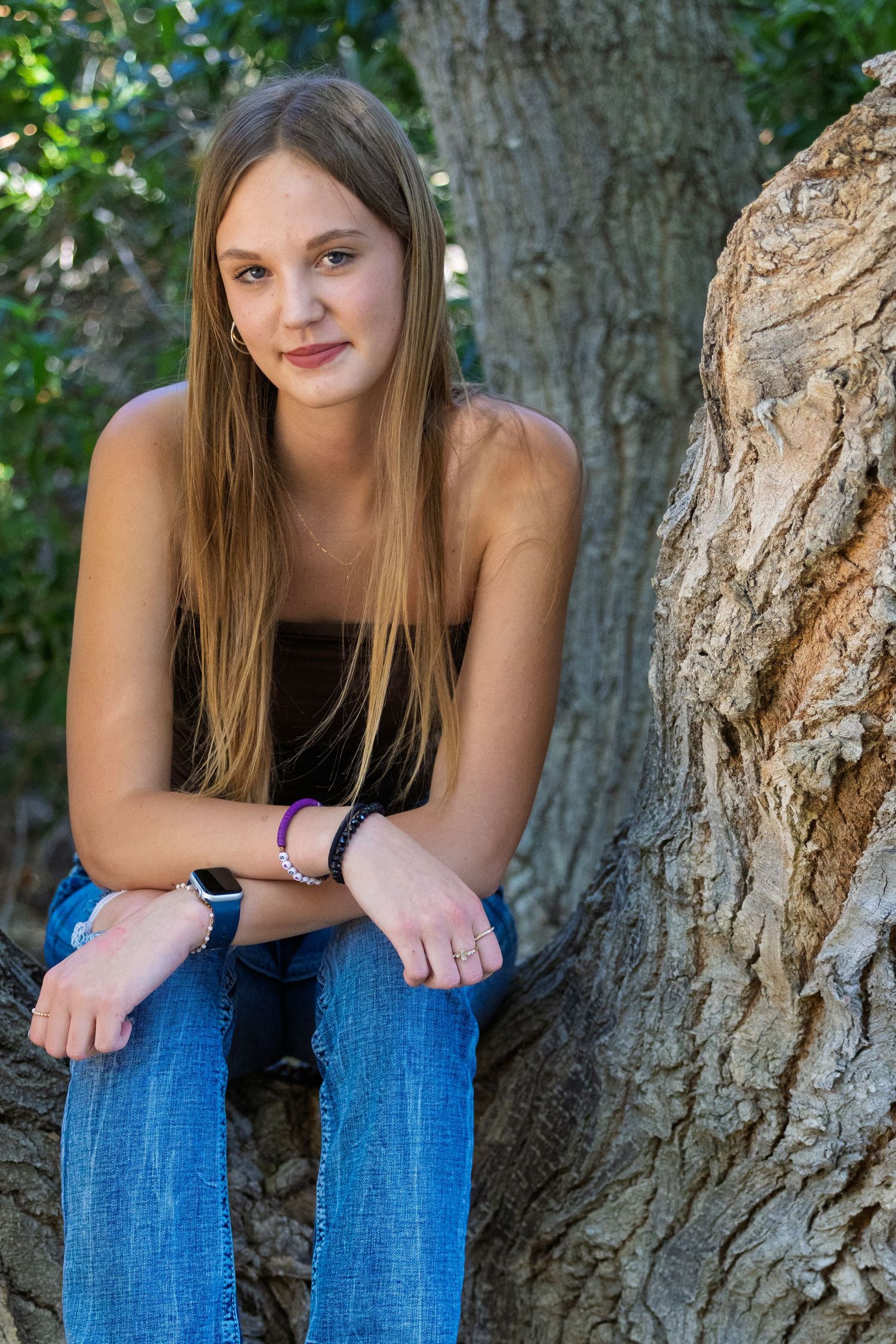 A young person in casual attire sits against a large tree trunk in a natural outdoor setting.