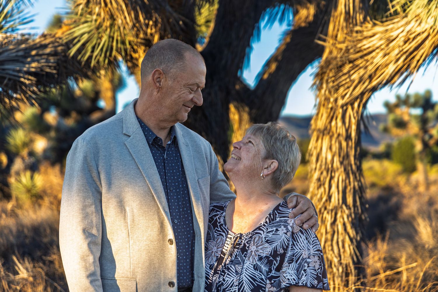 A couple shares a romantic moment at sunset in a desert landscape with Joshua trees.