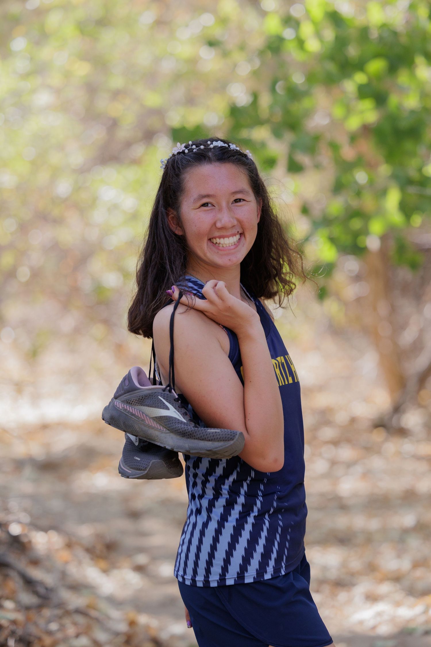 Person in navy striped tank top holding running shoes outdoors with natural background.