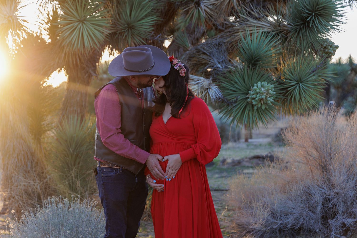 A romantic sunset portrait of a couple embracing near desert plants with sunlight streaming through.
