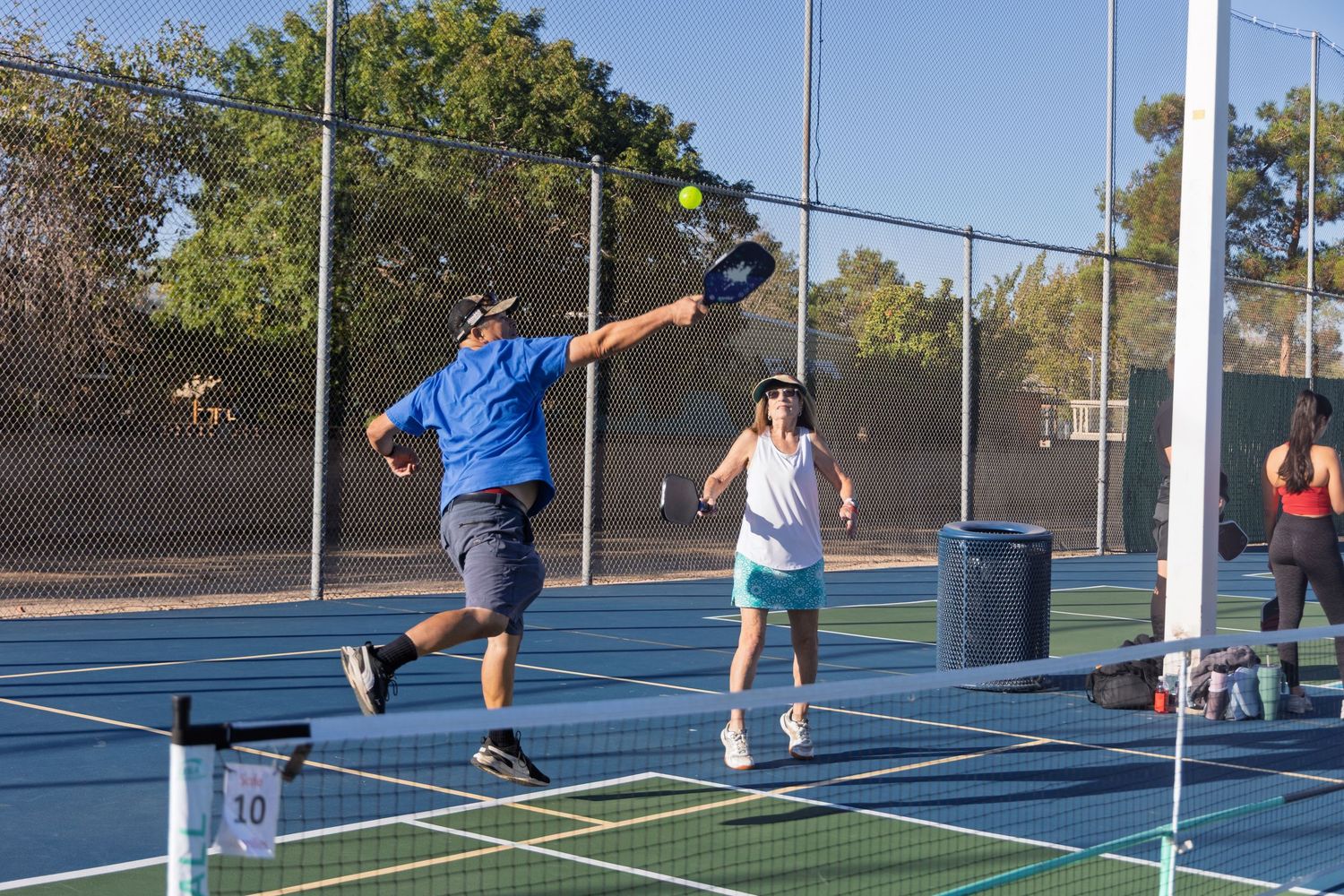 Sequence of pickleball players demonstrating proper serving technique on outdoor blue courts.