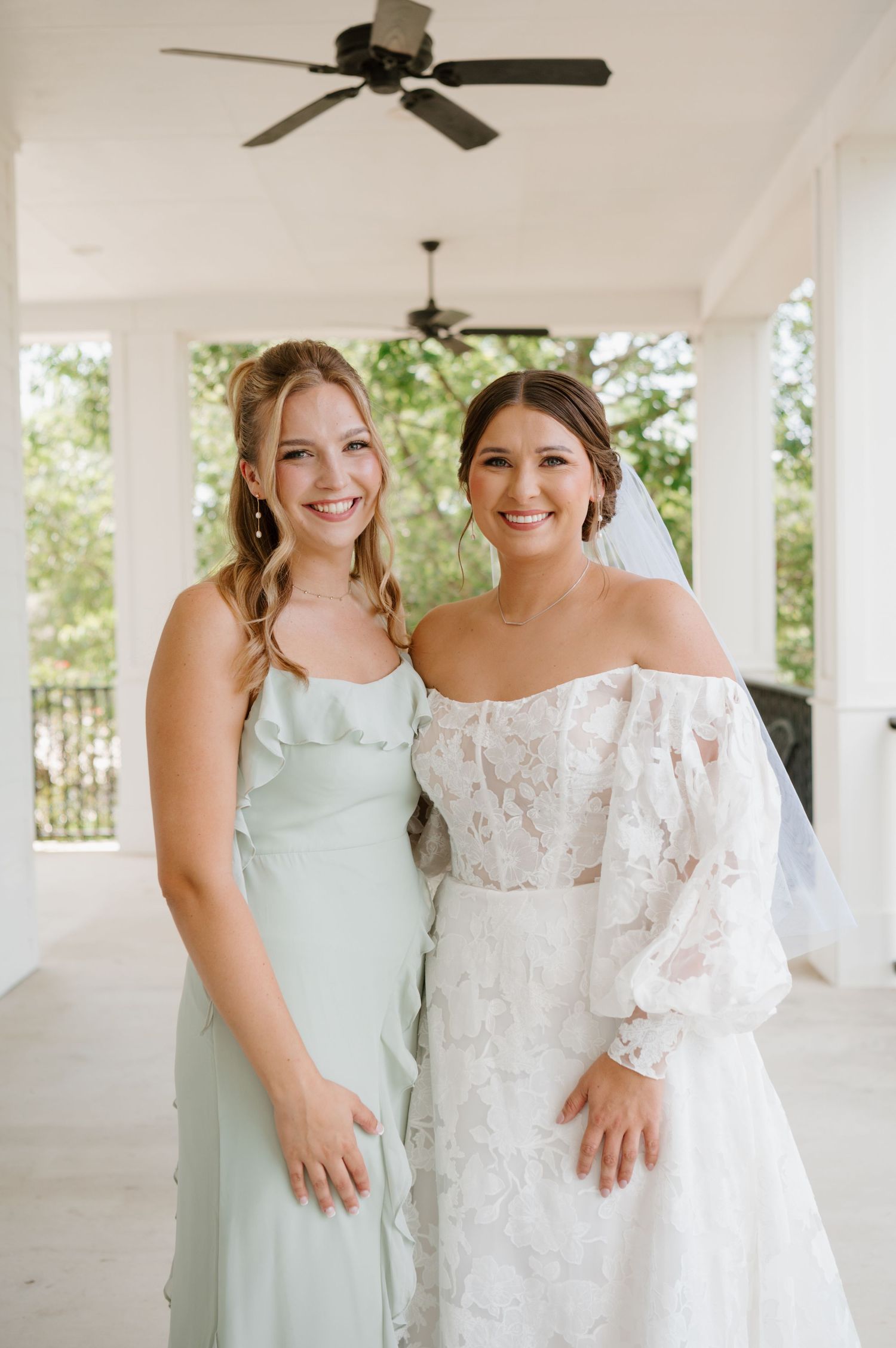 Bridal party members pose in white lace and mint green dresses on a covered outdoor porch.