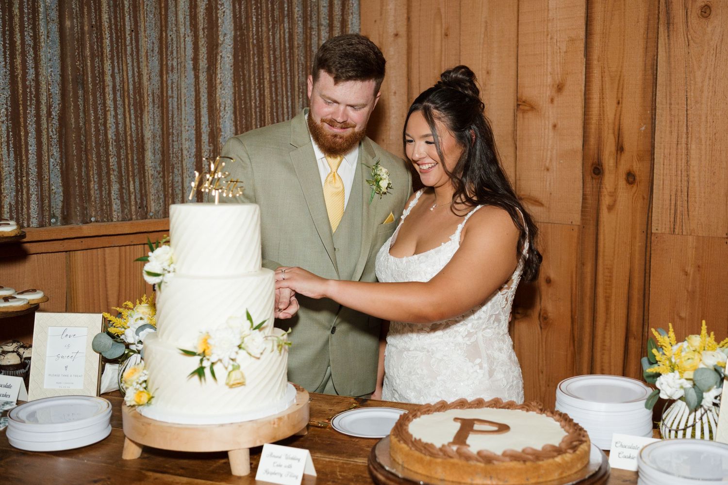Bride and groom cutting white tiered wedding cake with P monogram groom's cake beside it.