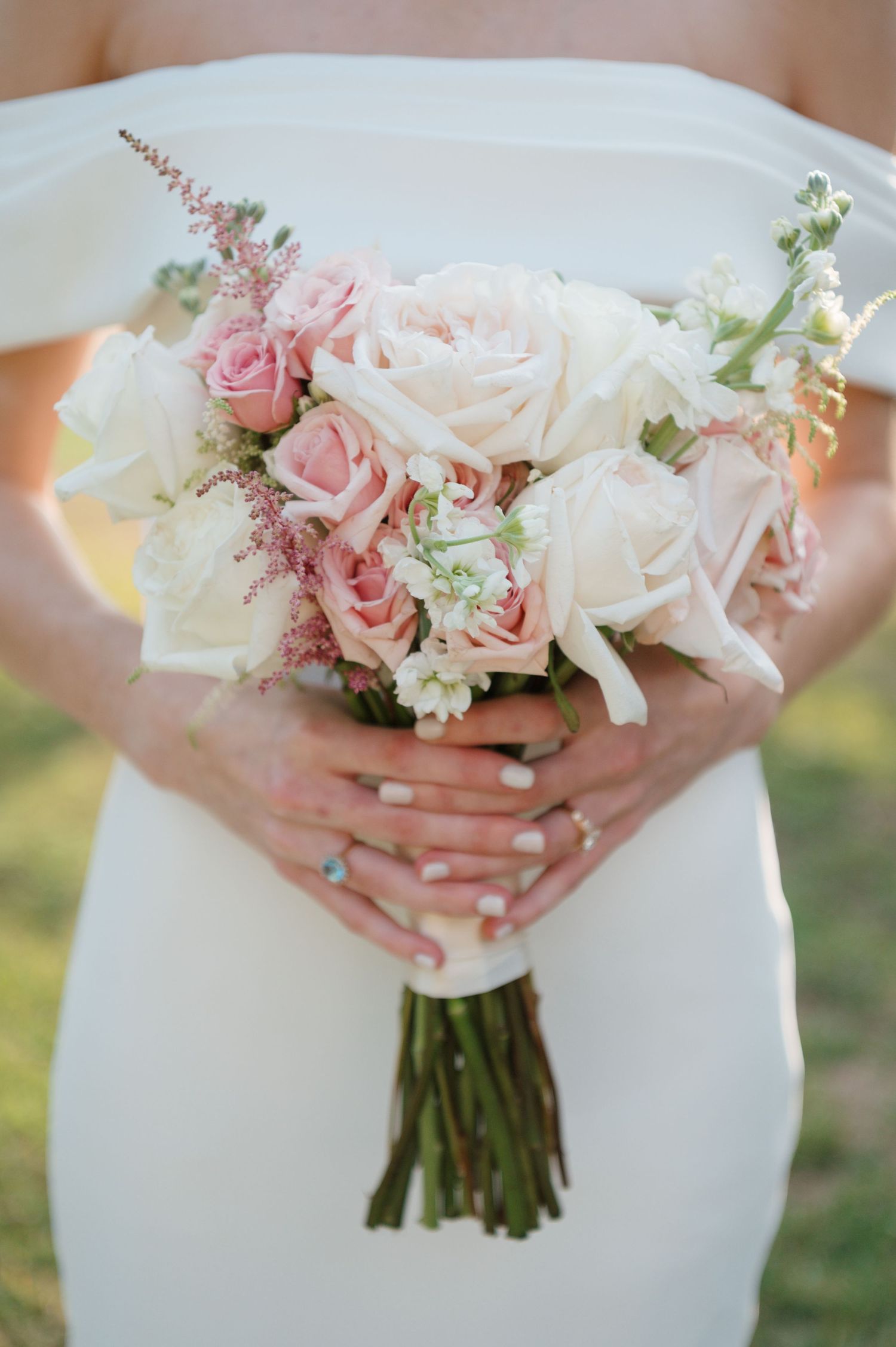 Close-up series of delicate pink and white wedding bouquet with roses held against a white dress.
