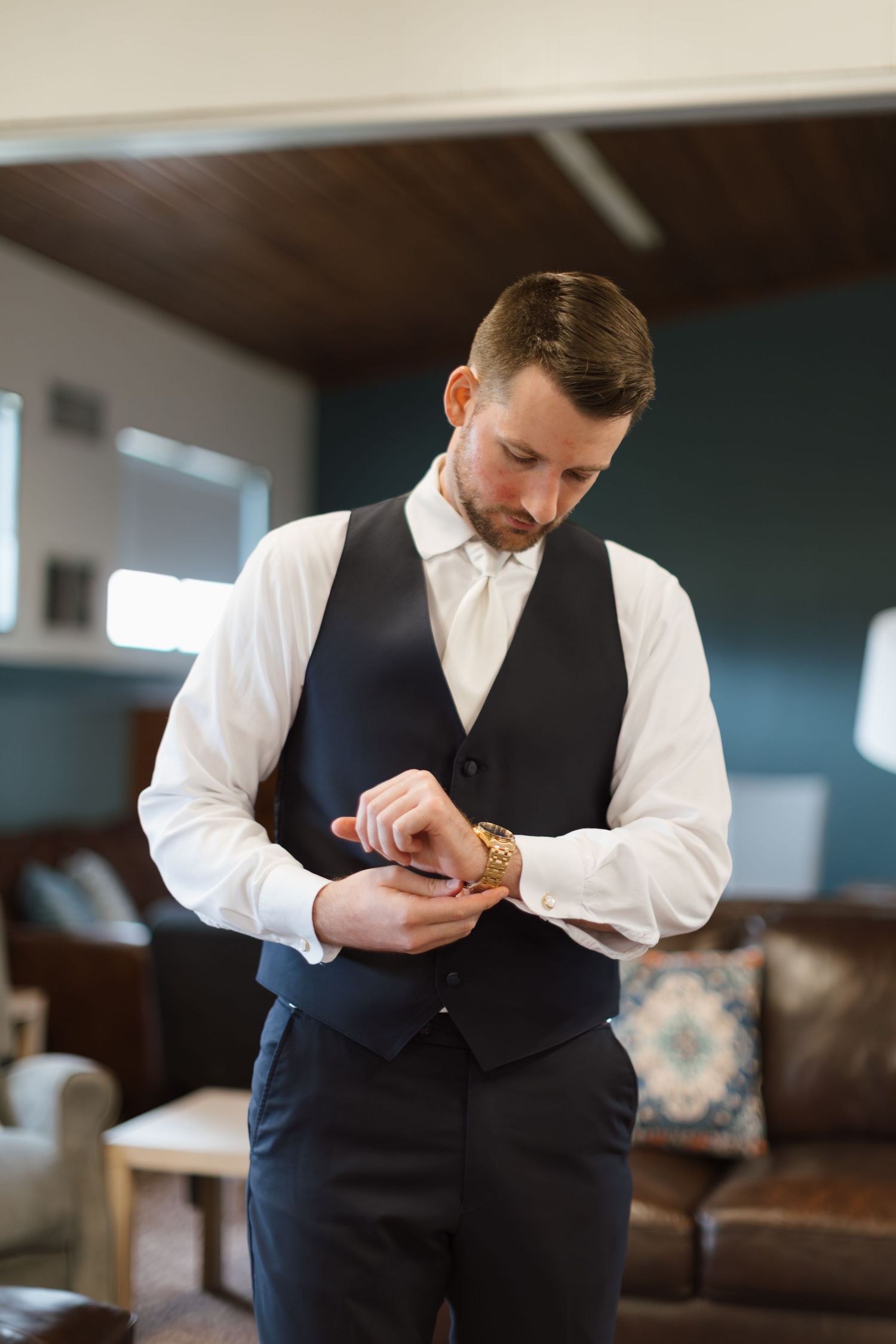 Person in formal attire adjusts their outfit while getting ready indoors with leather furniture in background.