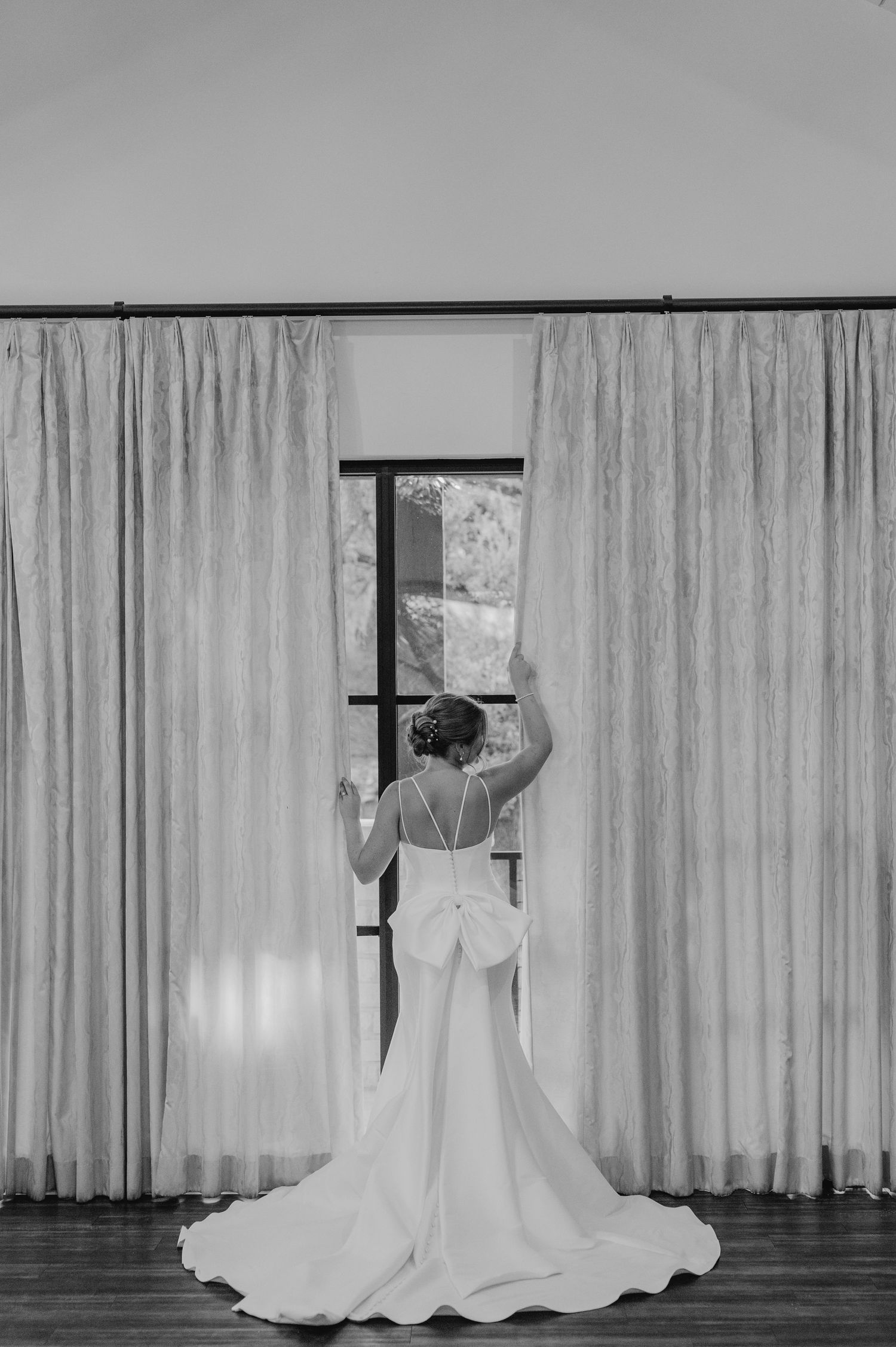 A dramatic black and white silhouette of a wedding dress train flowing across a light-filled room.