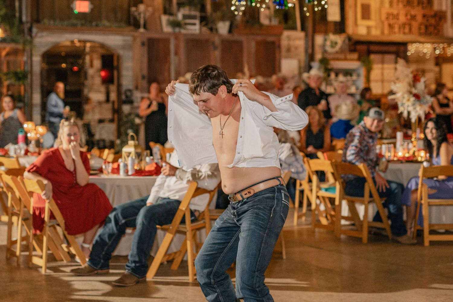 Wedding guests dancing at rustic indoor reception venue with string lights.