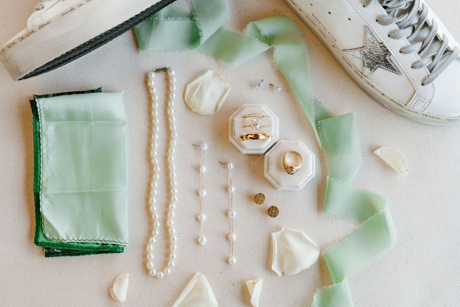 Elegant wedding accessories including pearls, mint green fabric, and delicate white lace ribbons arranged on light surface.