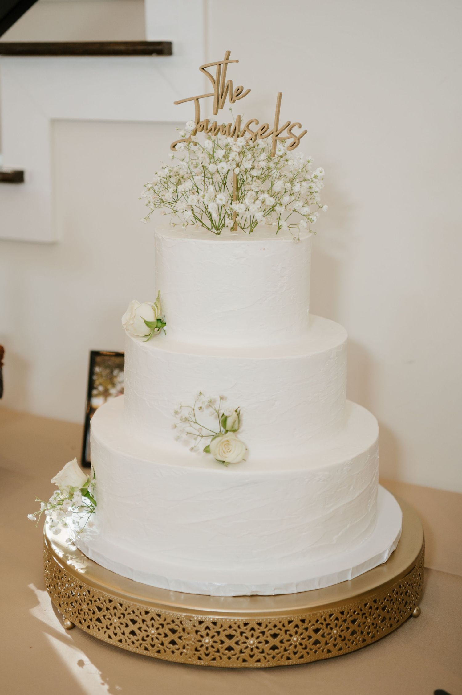Elegant white wedding cake with gold accents and delicate floral decorations displayed on a metallic stand.