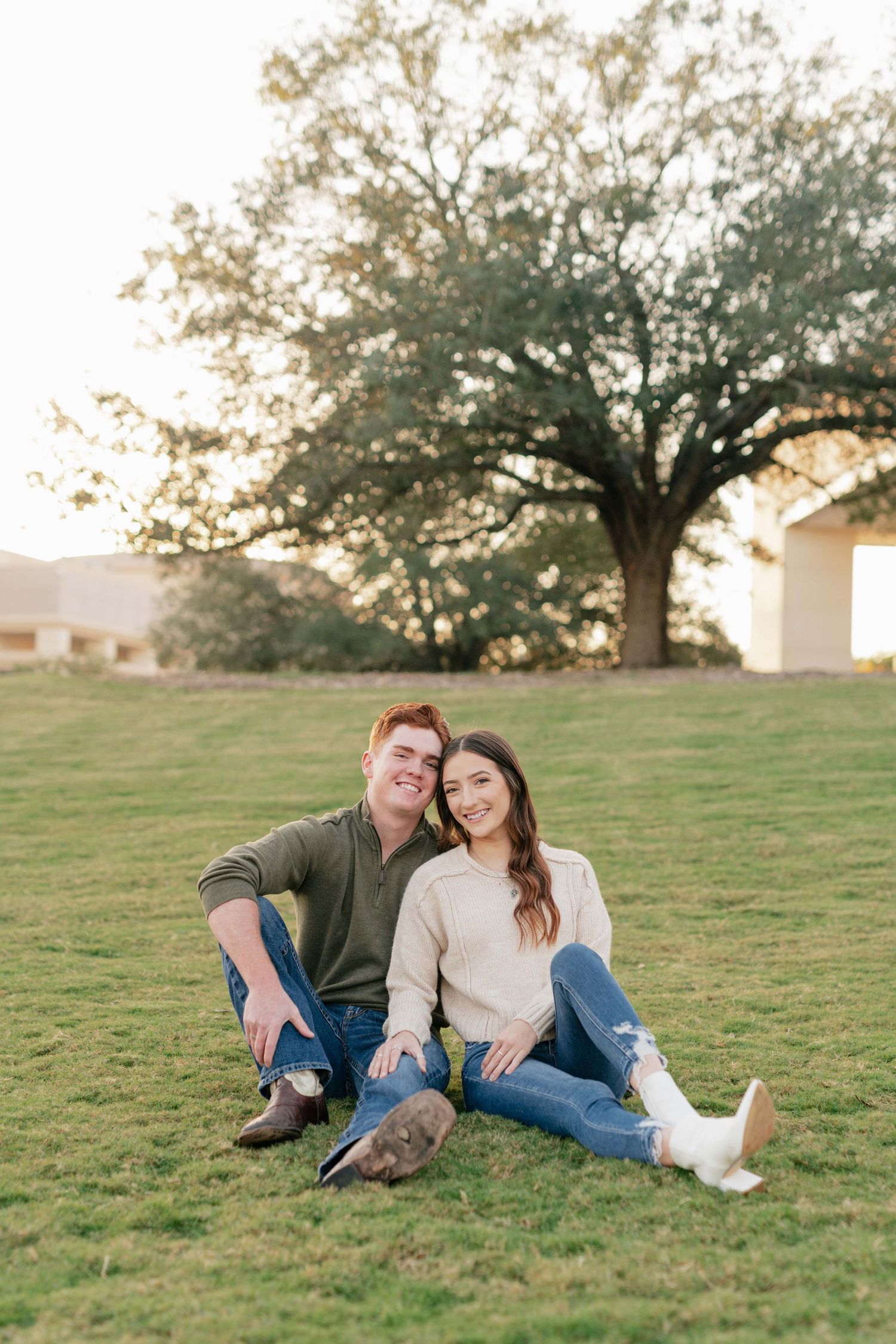 Casual couple sitting together on grassy hill during golden hour photo session.