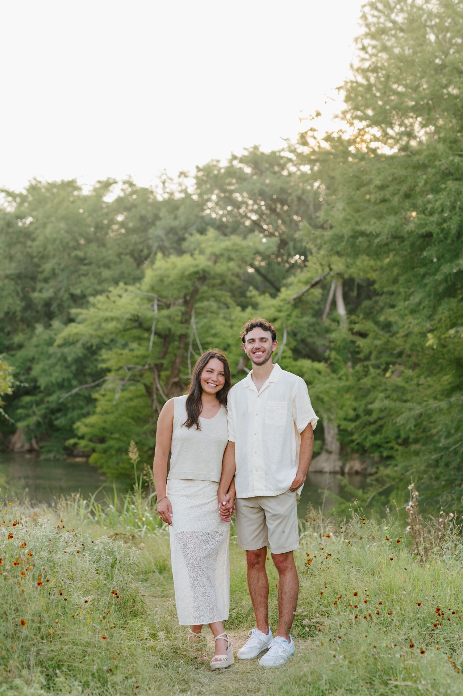 Couple wearing coordinated white outfits poses in a wildflower meadow during summer.