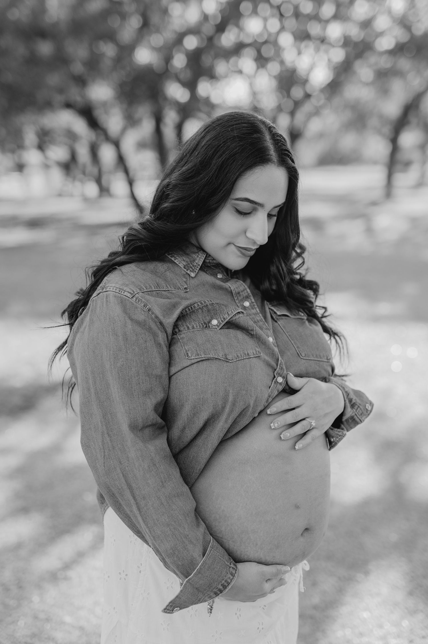 Black and white photo of an expectant mother holding her belly in a peaceful outdoor setting.