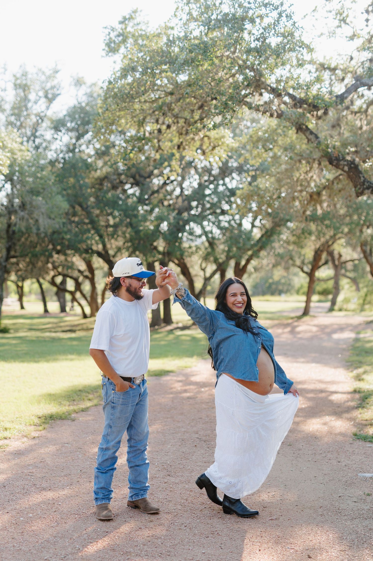 A romantic outdoor photoshoot showing a couple embracing and dancing on a dirt path surrounded by trees.