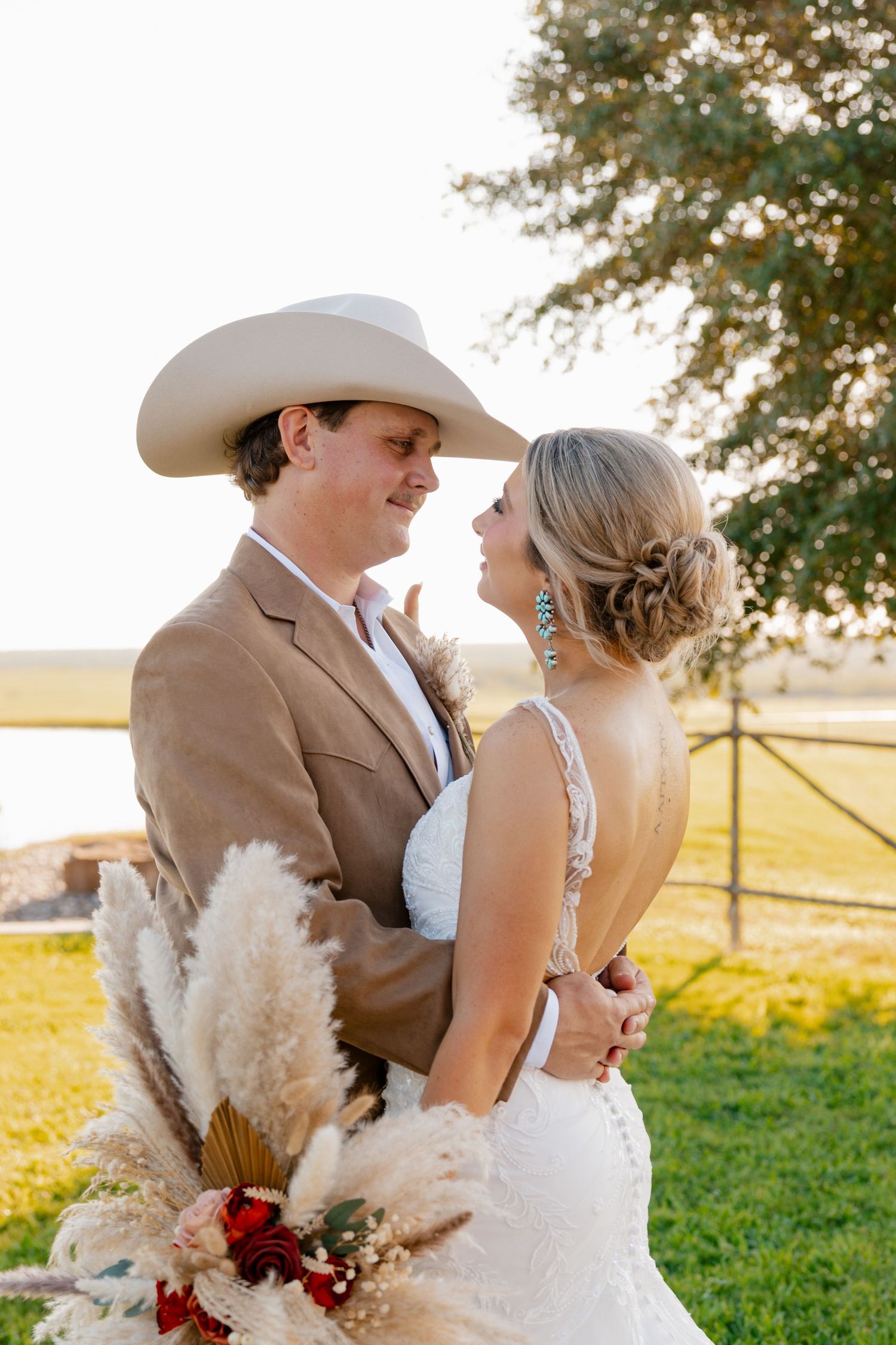 Romantic sunset portrait of western wedding couple with white cowboy hat against pastoral fence.