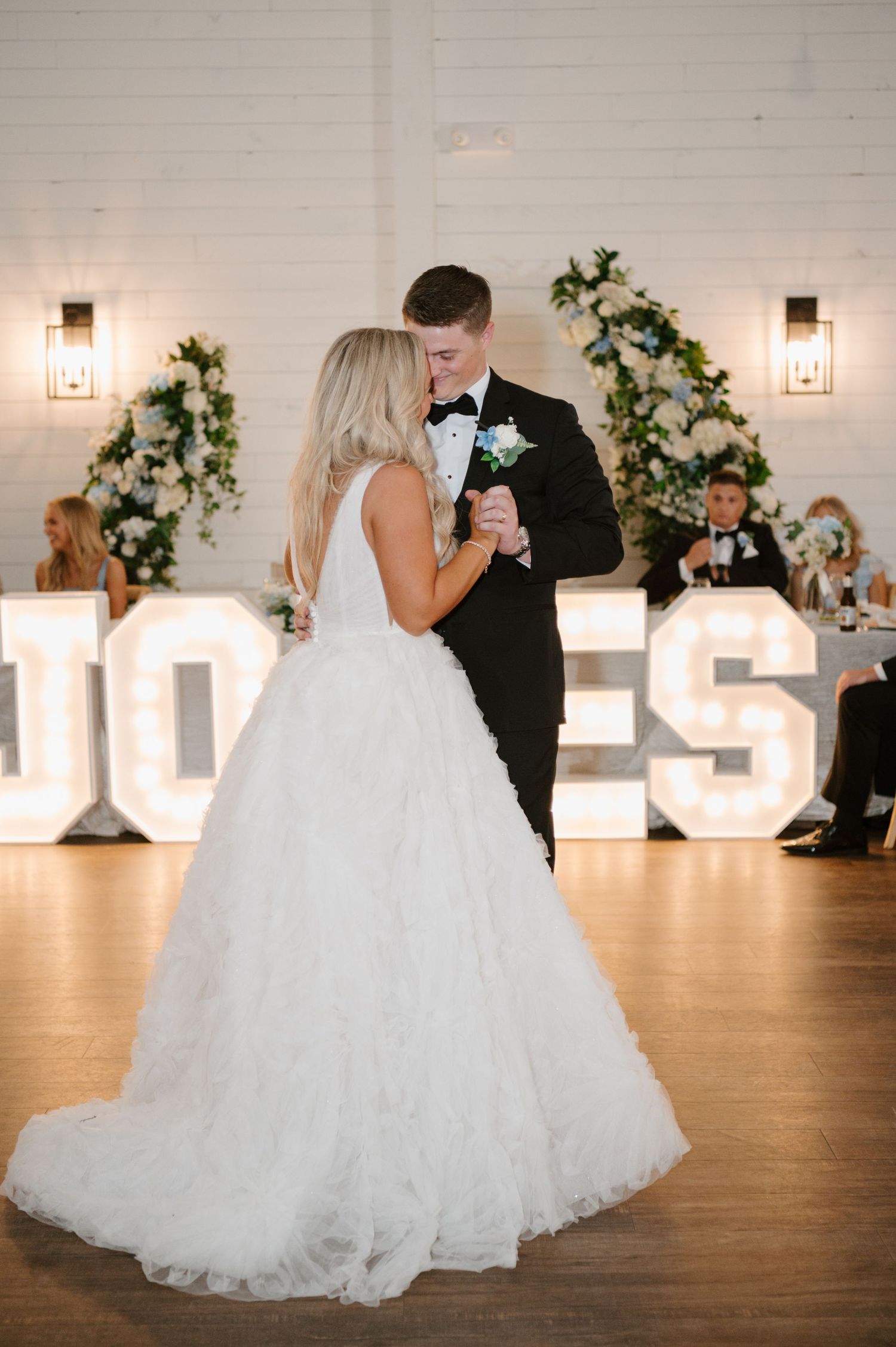 A bride in a white wedding dress is dancing with a man in a black tuxedo at a wedding reception.