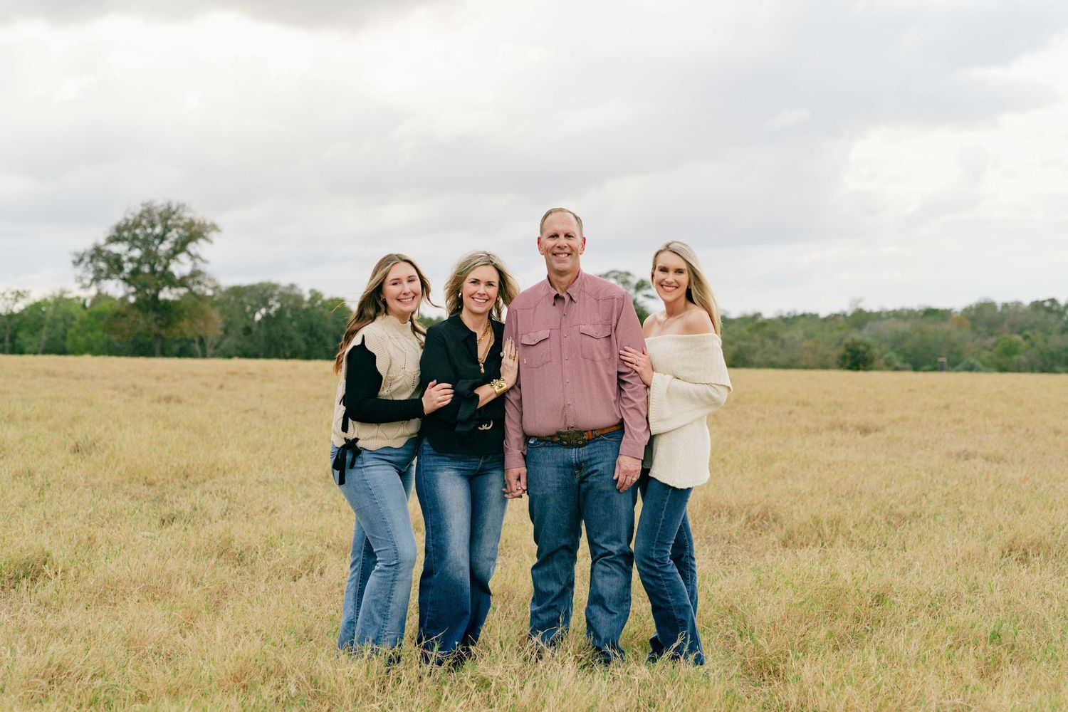 Family standing together in a sunny field wearing casual denim and neutral colors.