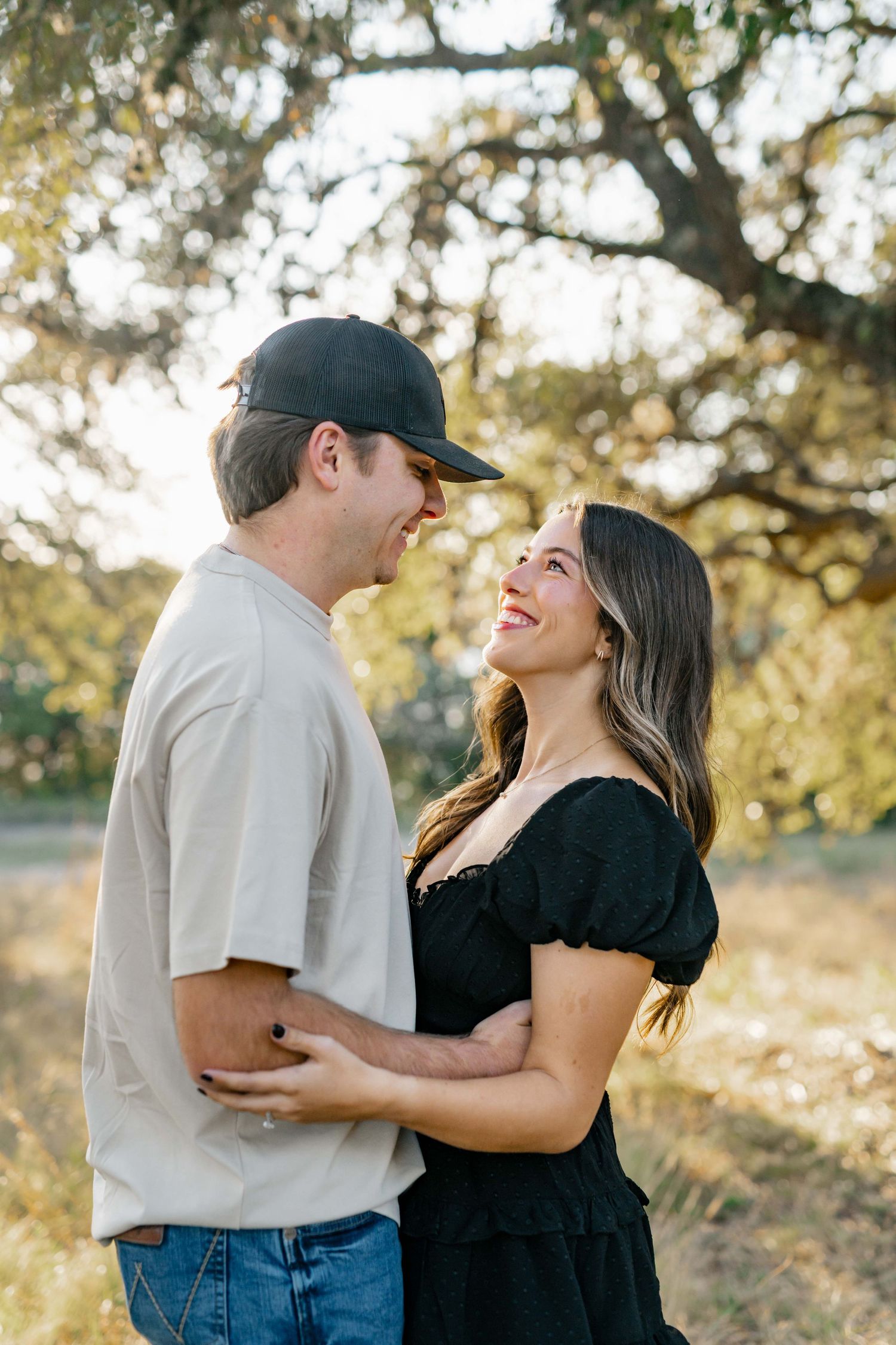 A couple shares an intimate moment while standing together in a sun-lit natural setting.