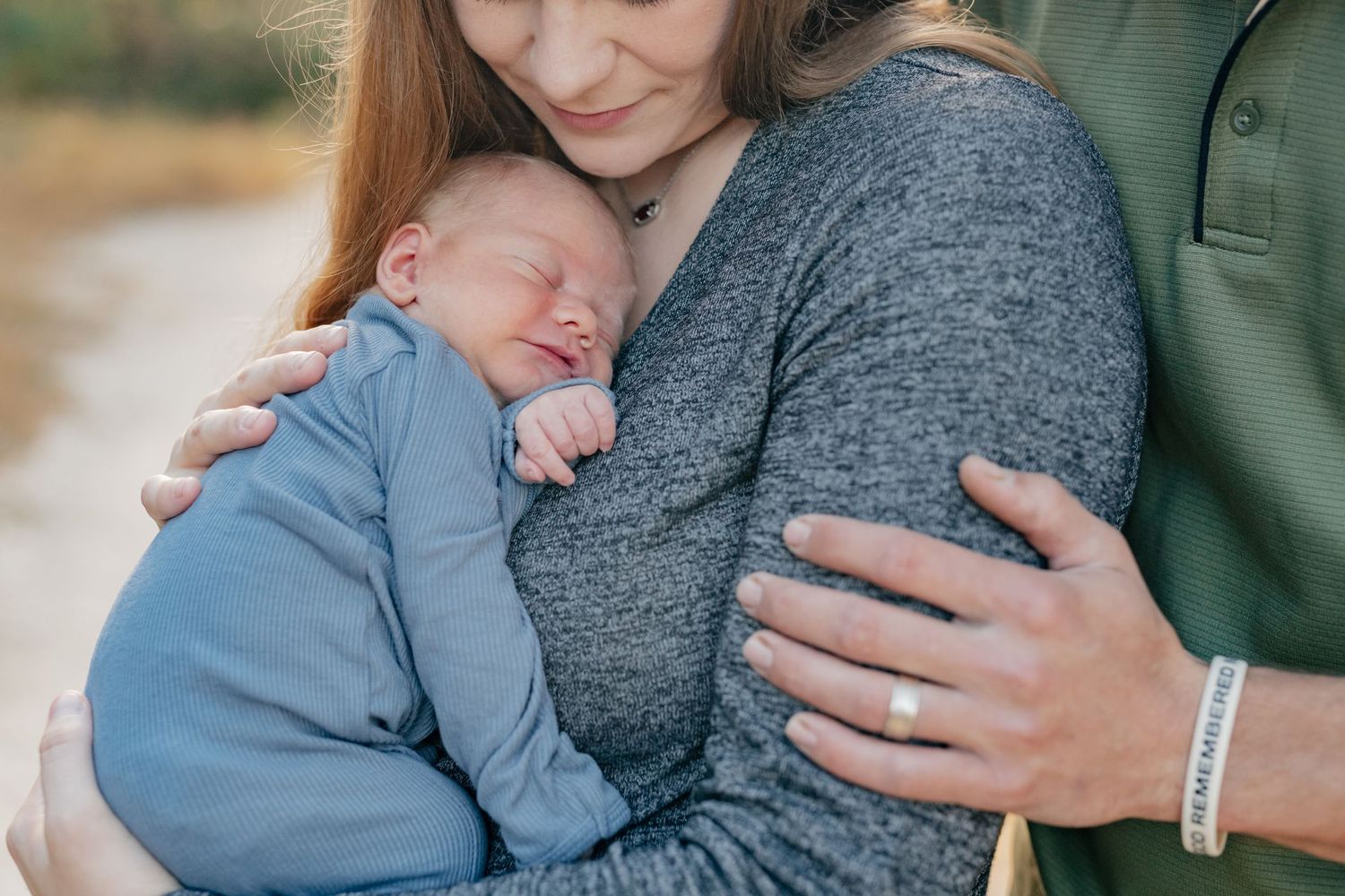 Close-up shot of sleeping baby in blue resting against mother's gray sweater.