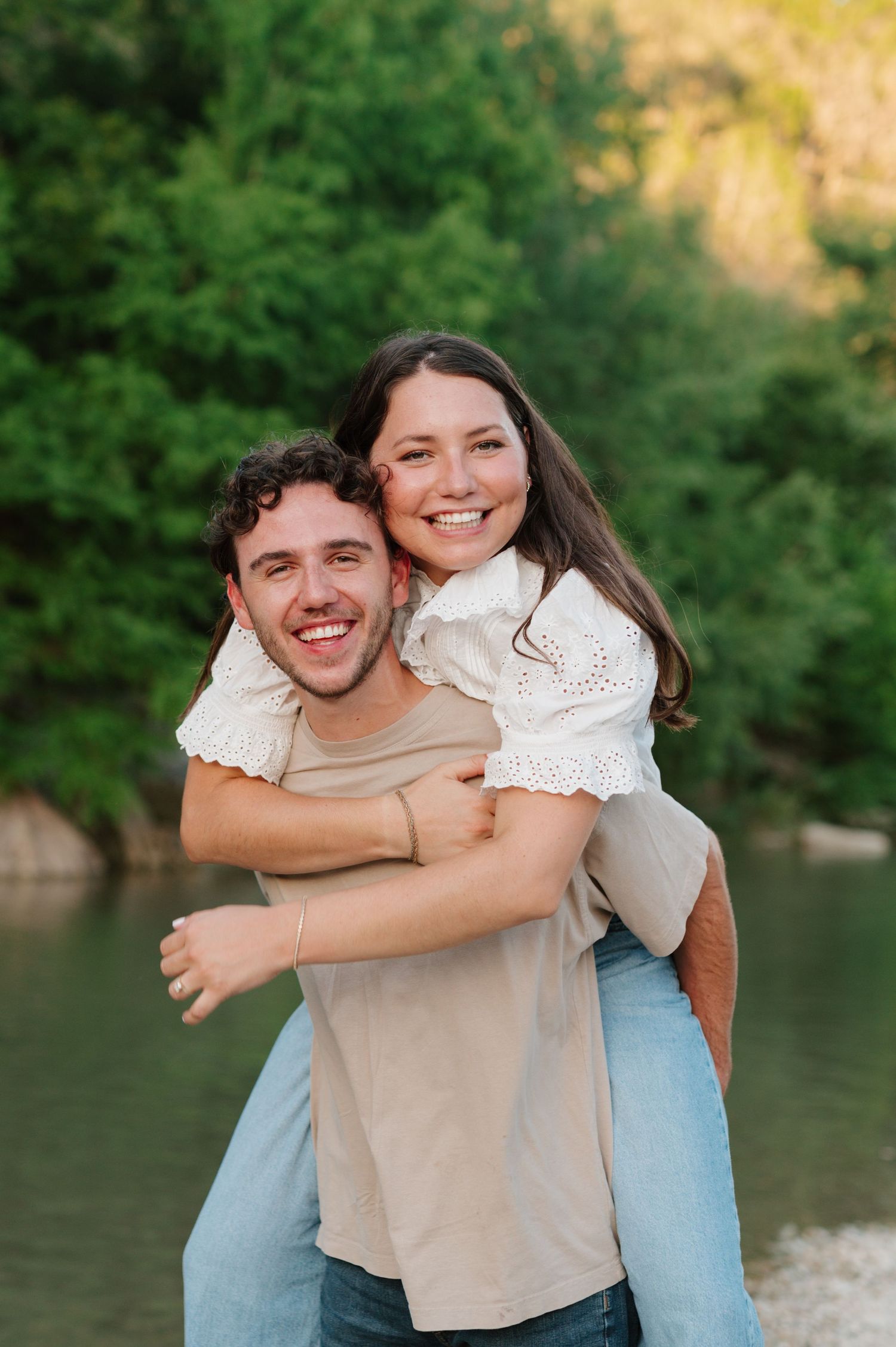 Joyful piggyback ride moment captured by water with lush greenery in background.