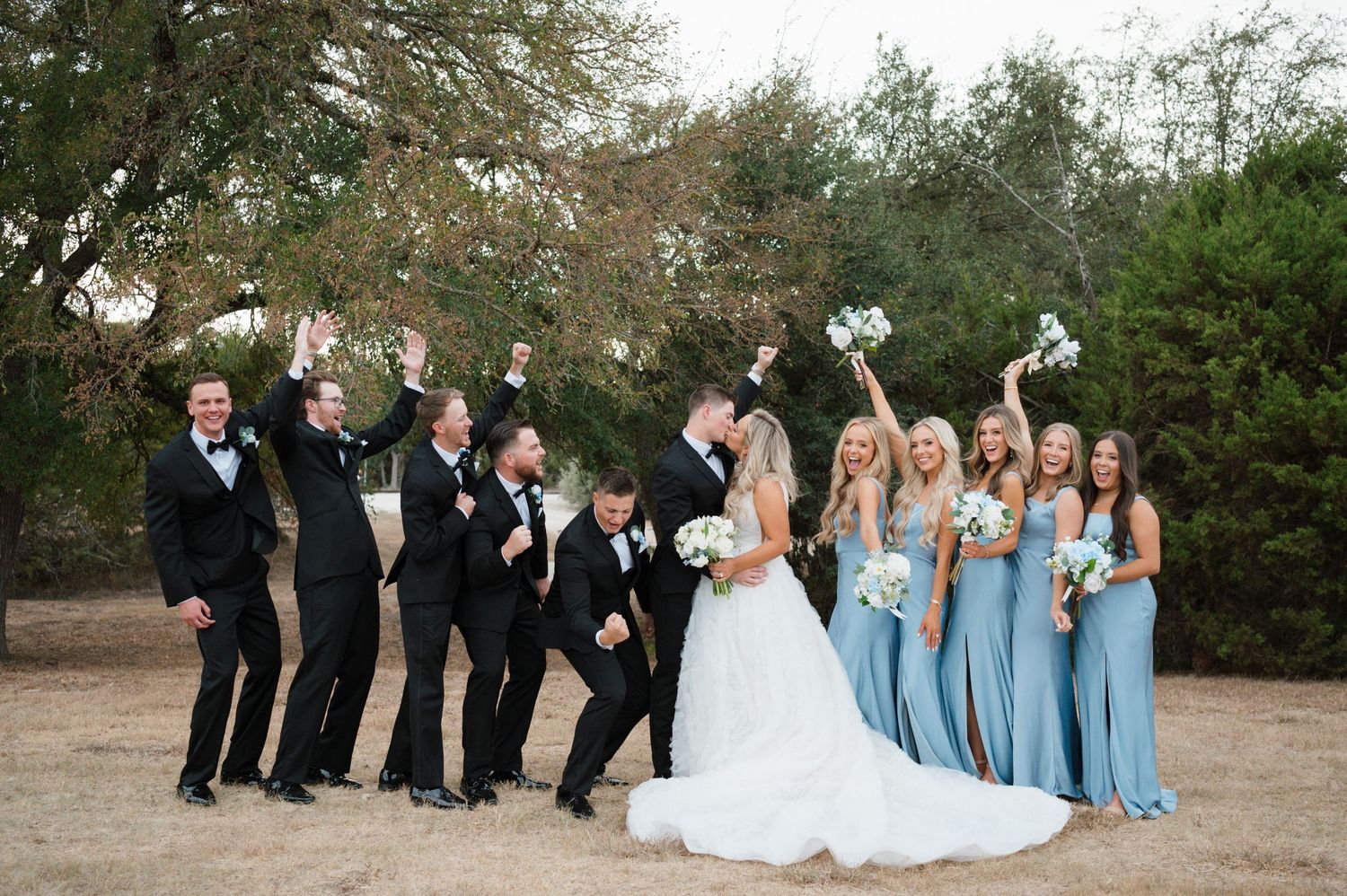 A bride and groom pose with their wedding party in a garden setting.