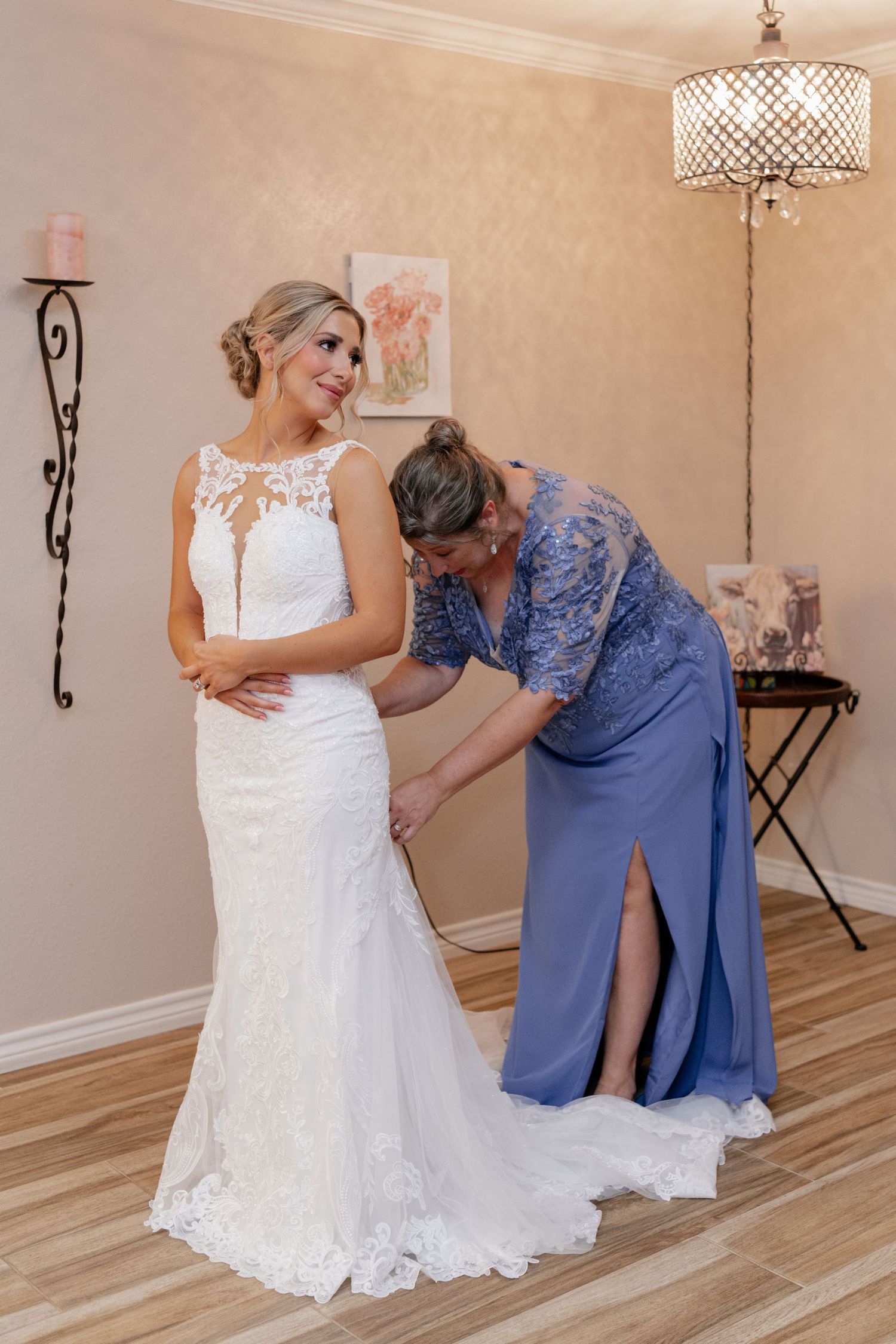 A wedding dress being adjusted in a room with a decorative chandelier and beige walls.