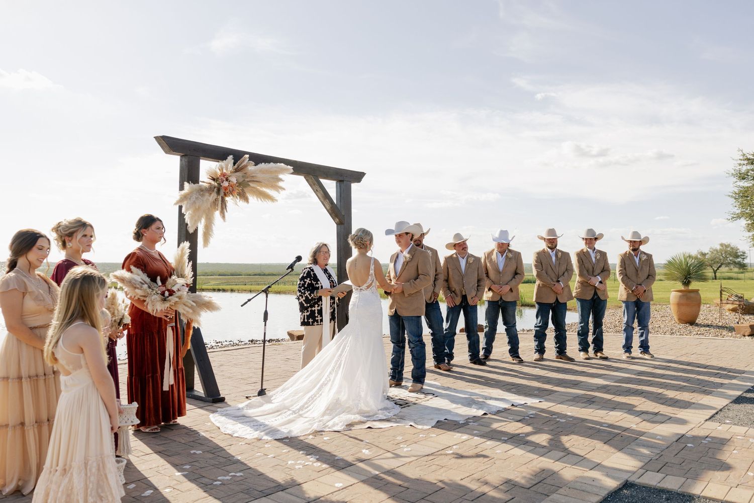Wedding ceremony at outdoor venue with bridal party lined up under wooden arch.