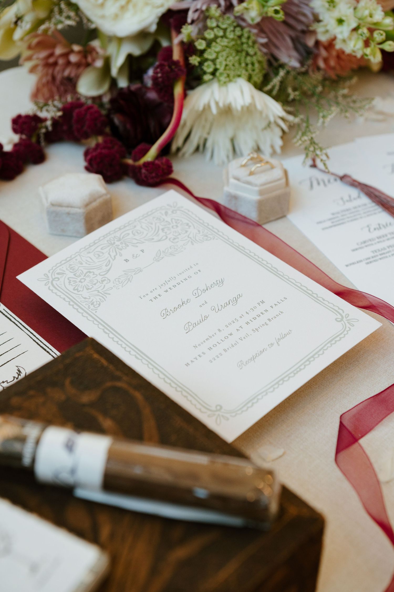 Elegant wedding invitation with burgundy border details displayed alongside floral arrangements and decorative elements.