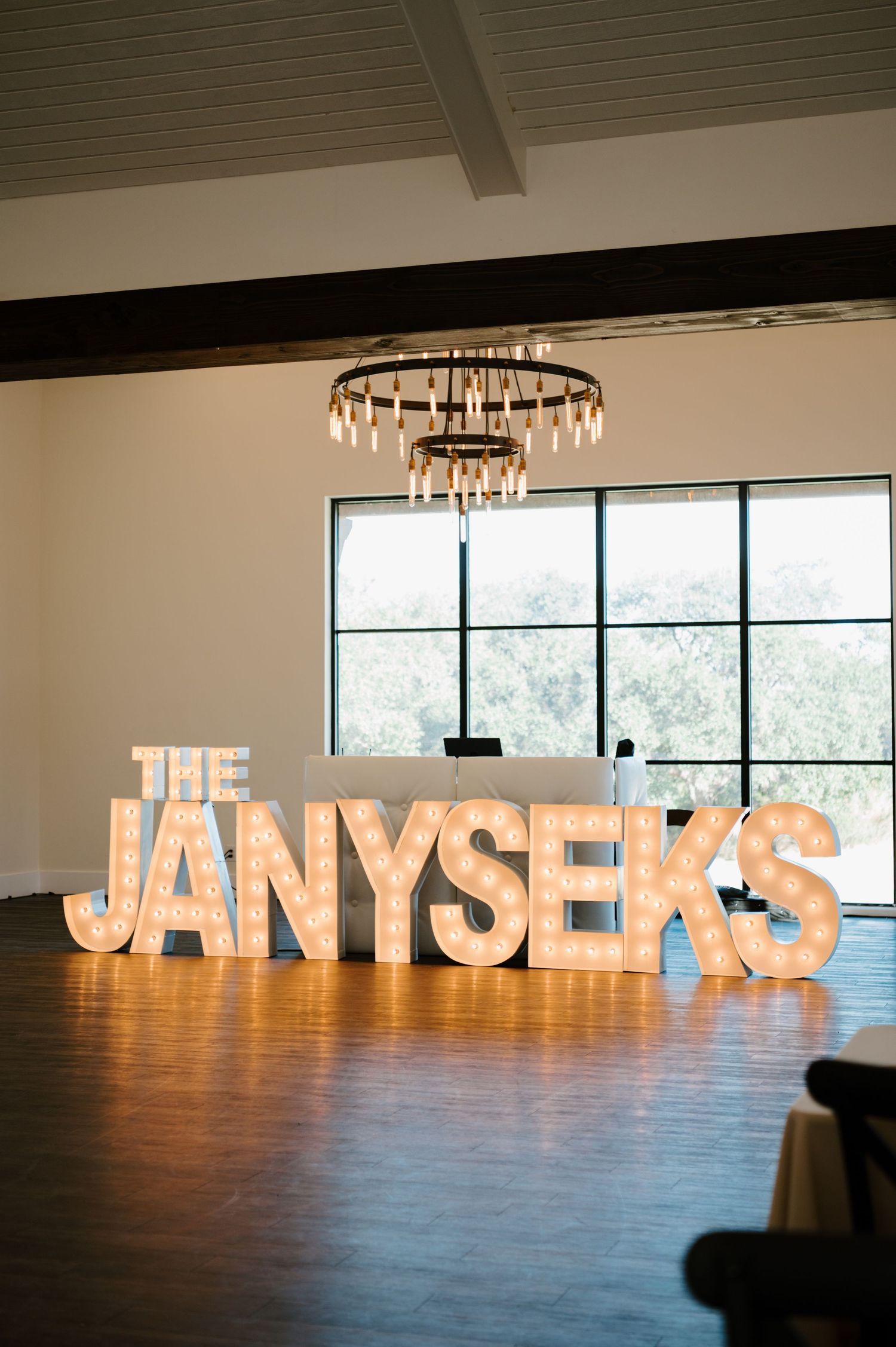 Large illuminated marquee letters spelling THE JANYSEKS under an elegant chandelier in an event space.