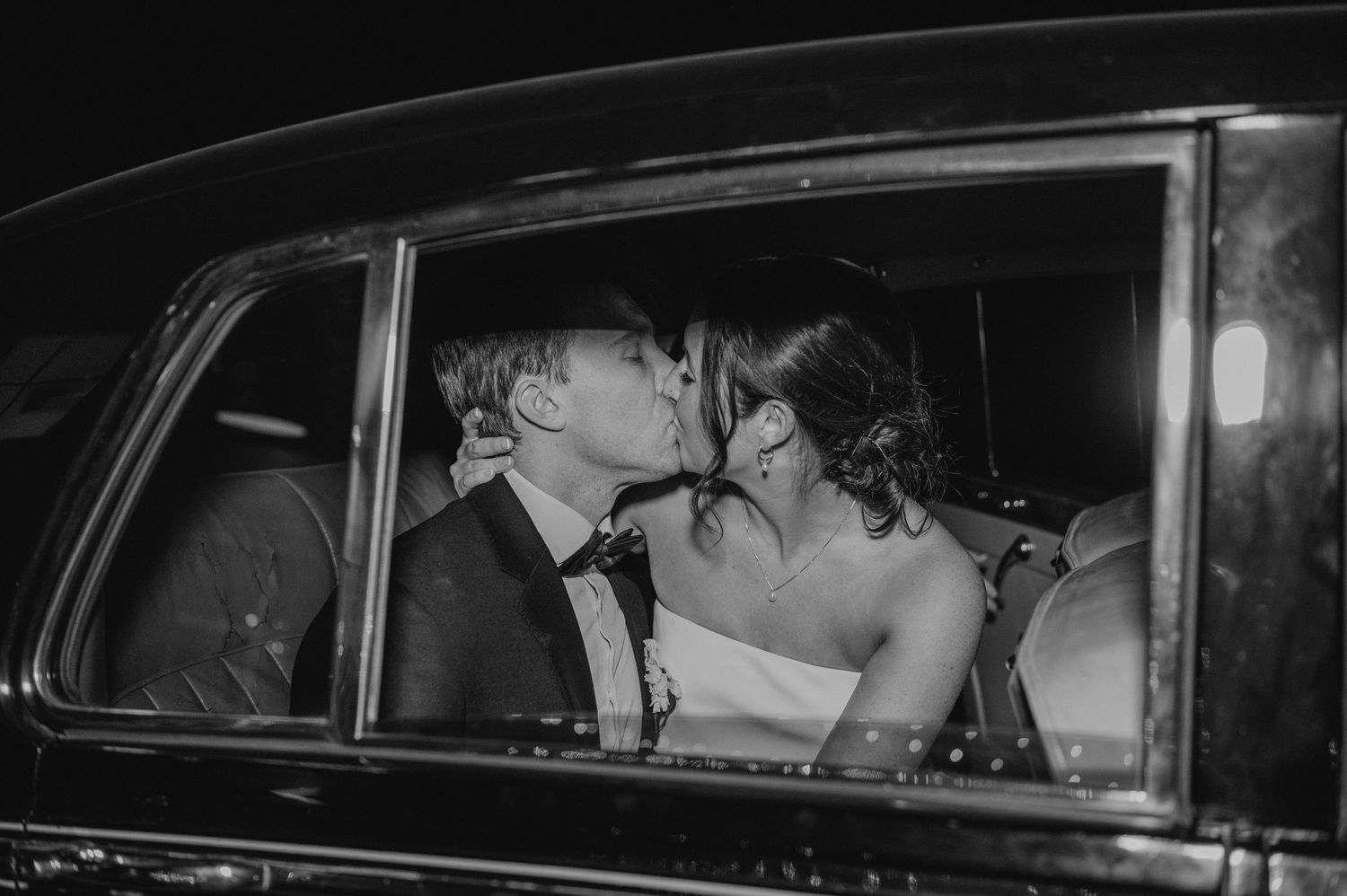 A vintage black and white photograph showing a car interior with occupants at night.