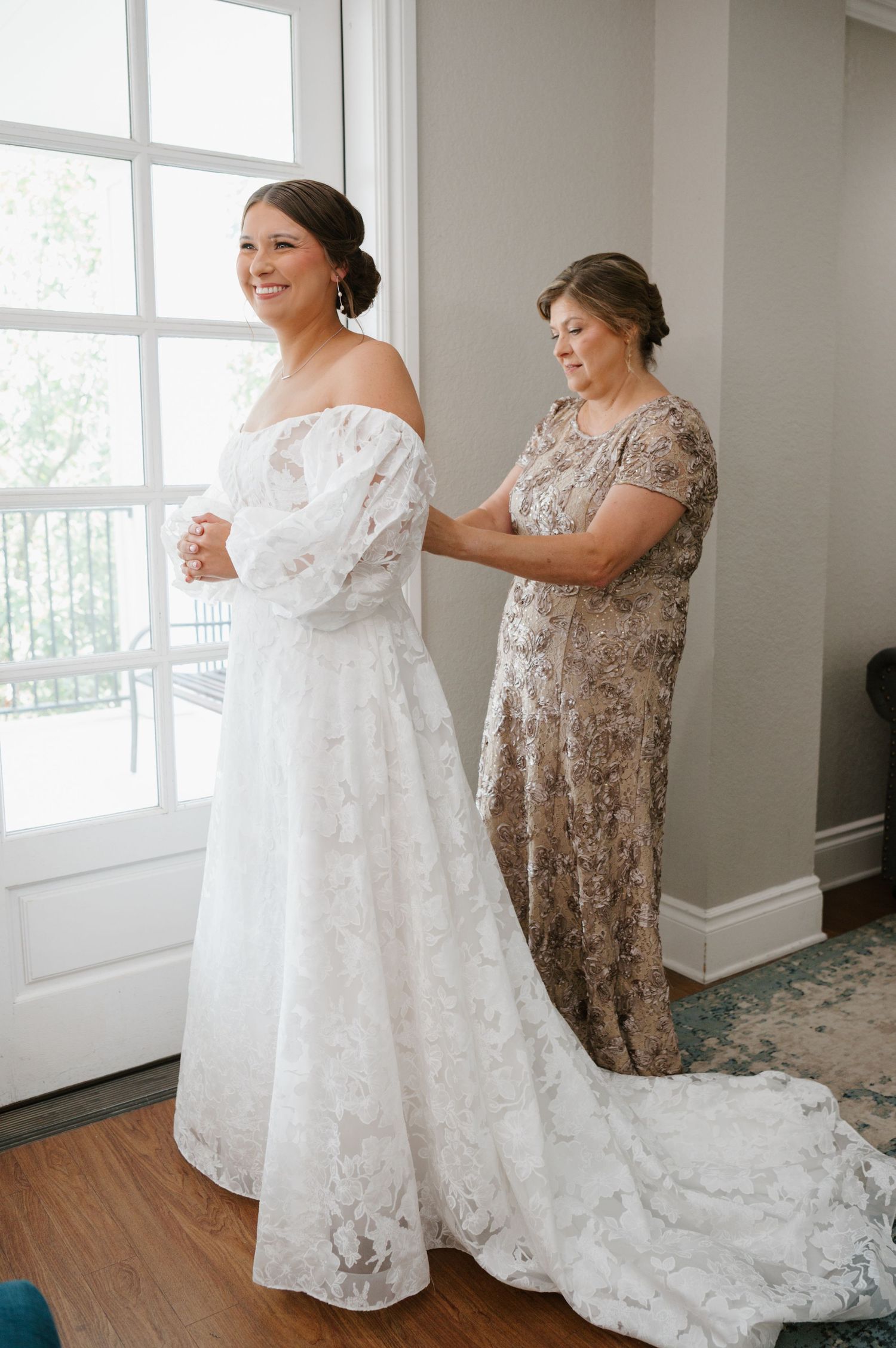 Beautiful lace wedding dress being fitted in a sunlit room.