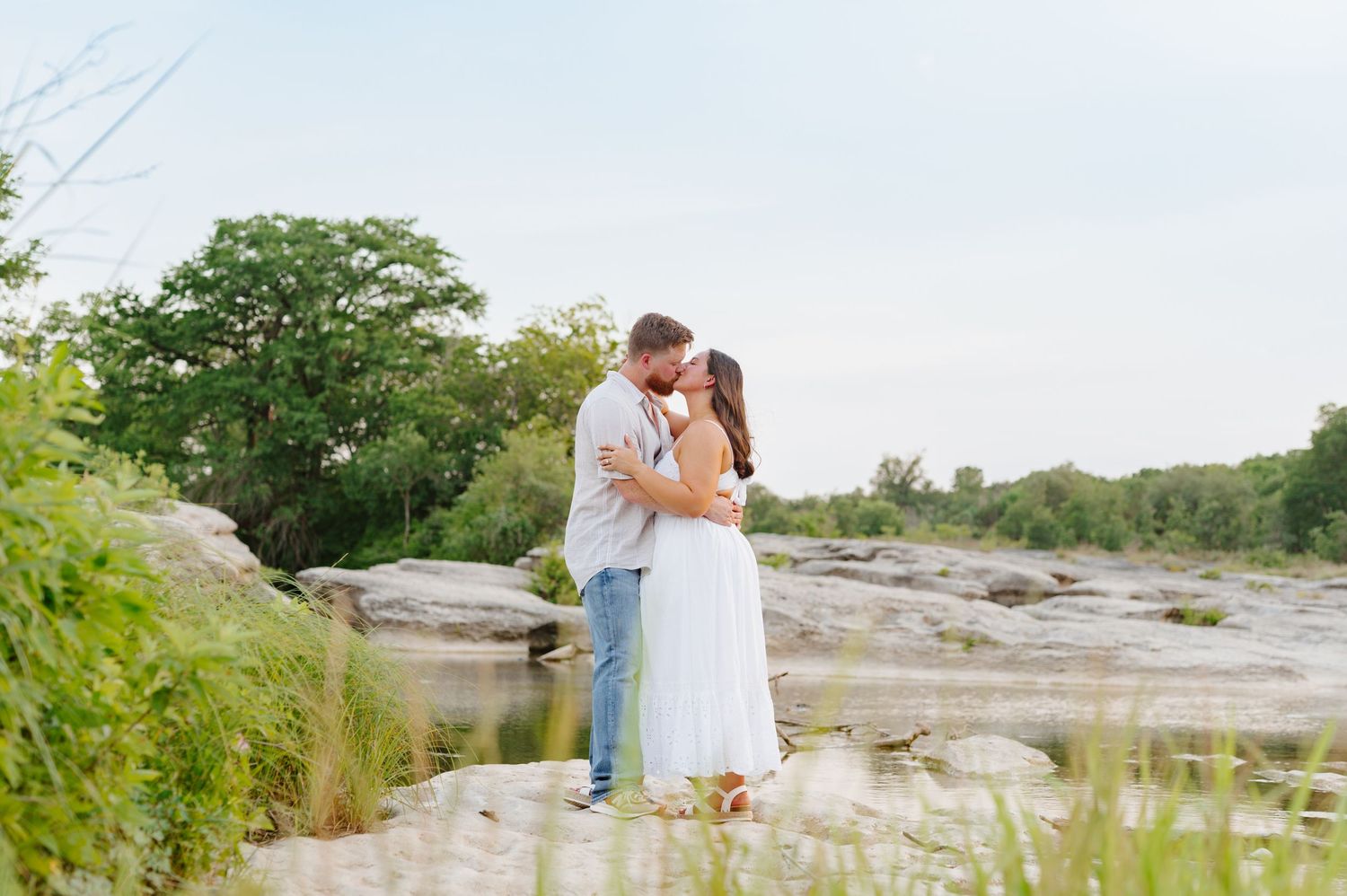 Scenic outdoor photoshoot by the water during a summer evening with a couple embracing.