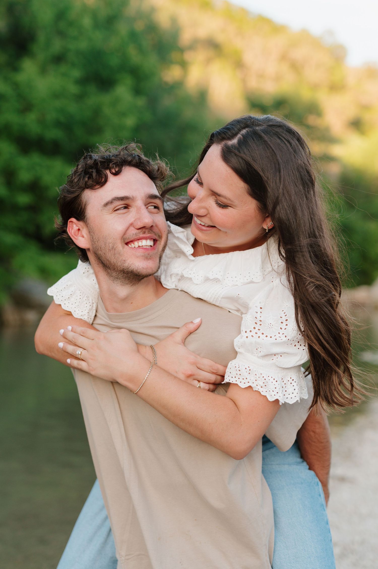 A joyful moment shared between a couple outdoors with sunlit greenery in the background.