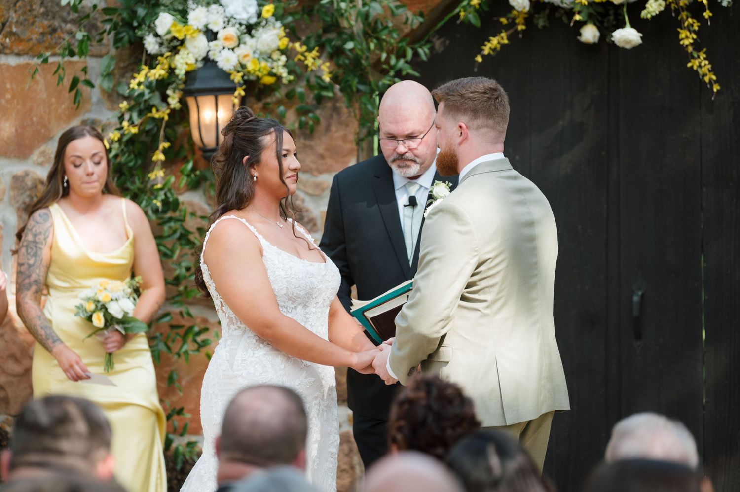 Bride and groom exchange vows at outdoor wedding ceremony with officiant and bridesmaid in yellow dress.