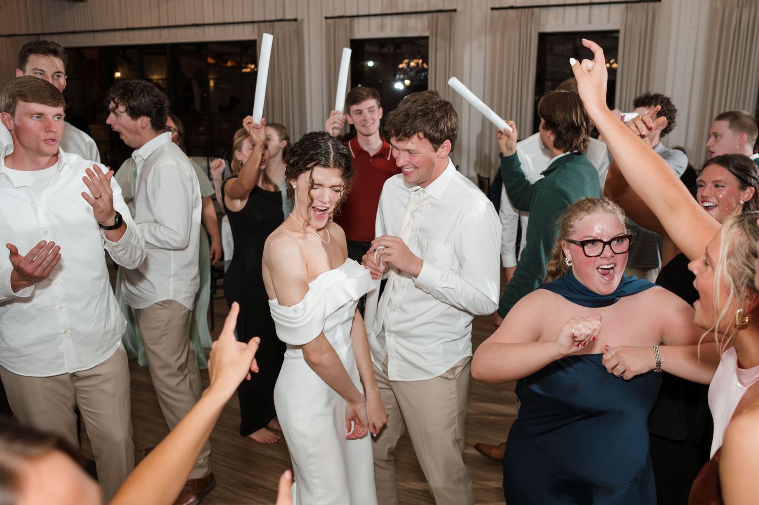 Wedding reception guests in white attire dancing and celebrating energetically on a crowded dance floor.