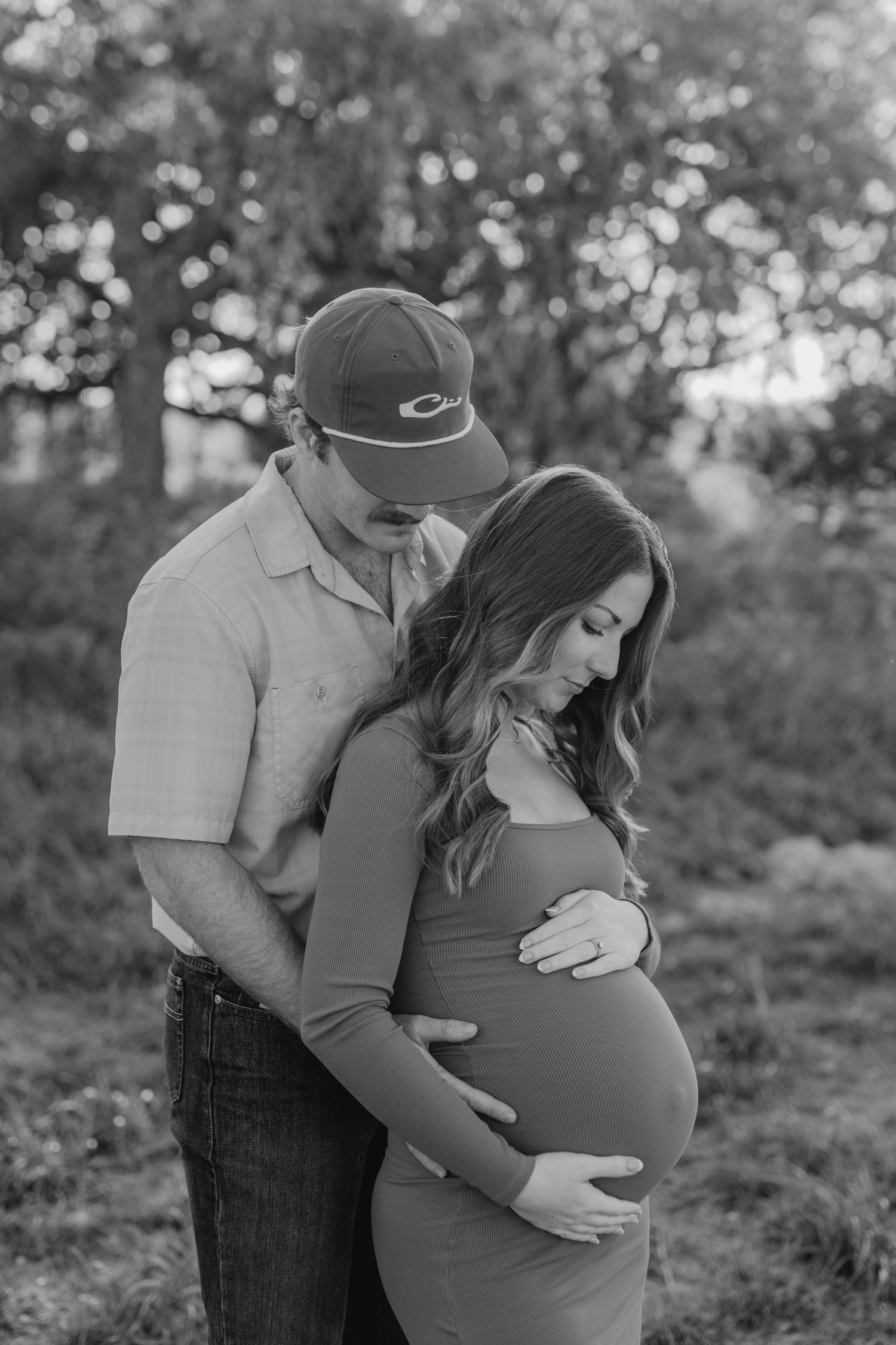 Intimate black and white maternity photo of a couple embracing outdoors with natural bokeh background.