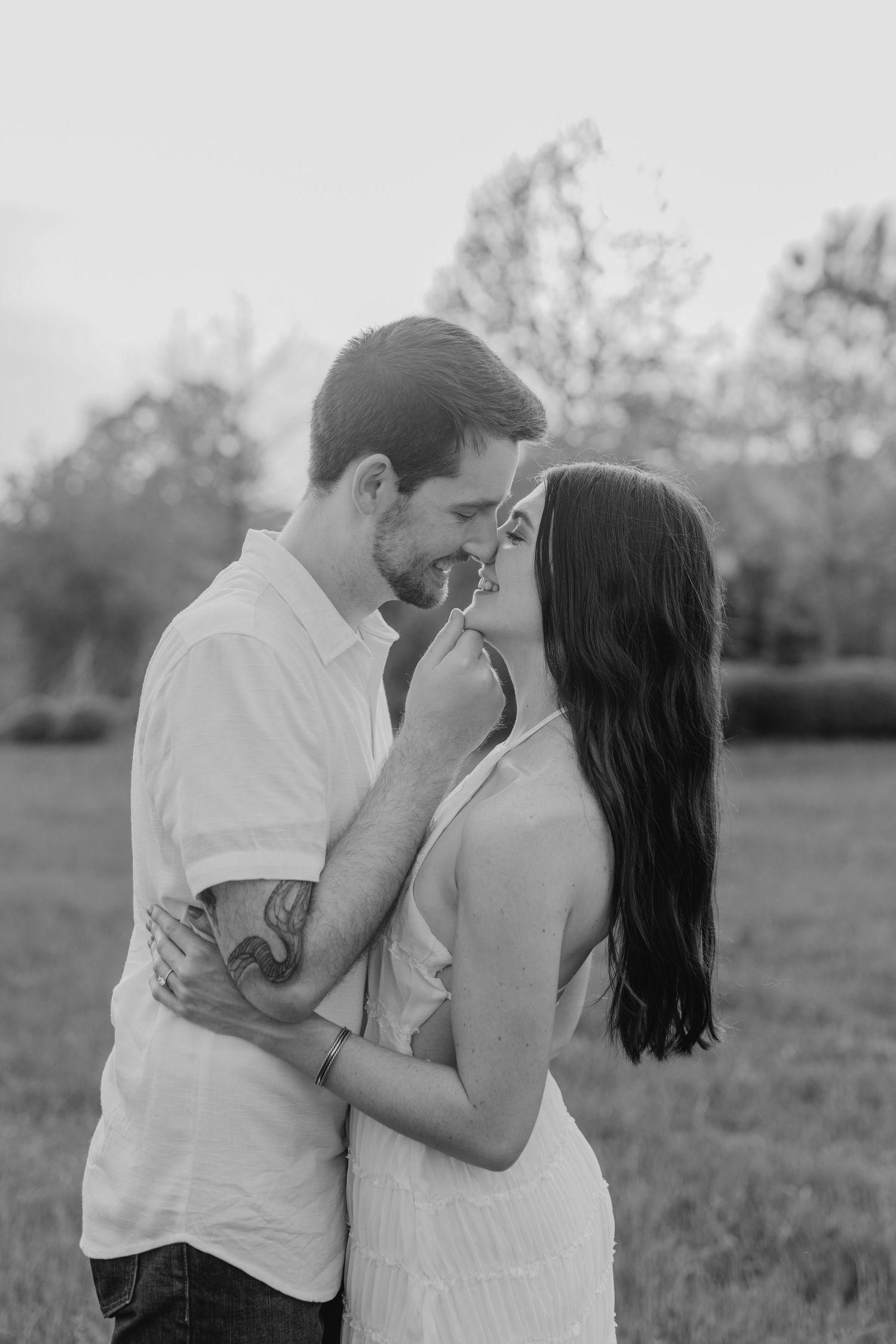 A romantic black and white outdoor portrait of a couple sharing an intimate moment in a natural setting.