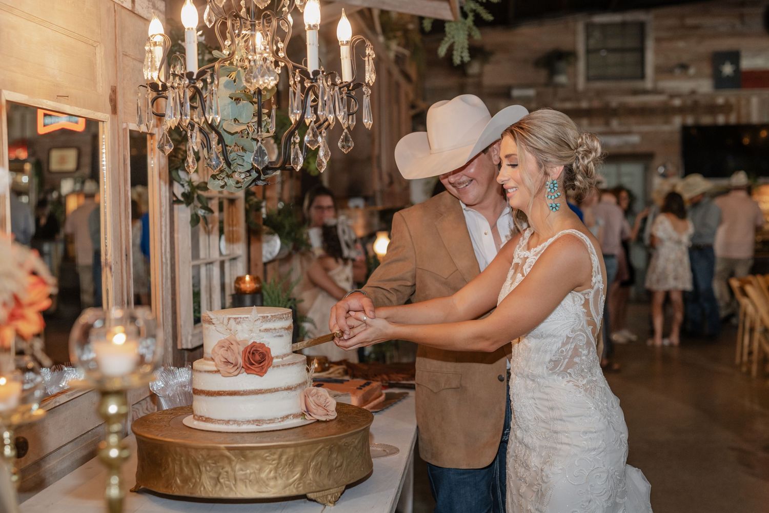 Newlyweds cut their elegant wedding cake together under a crystal chandelier.