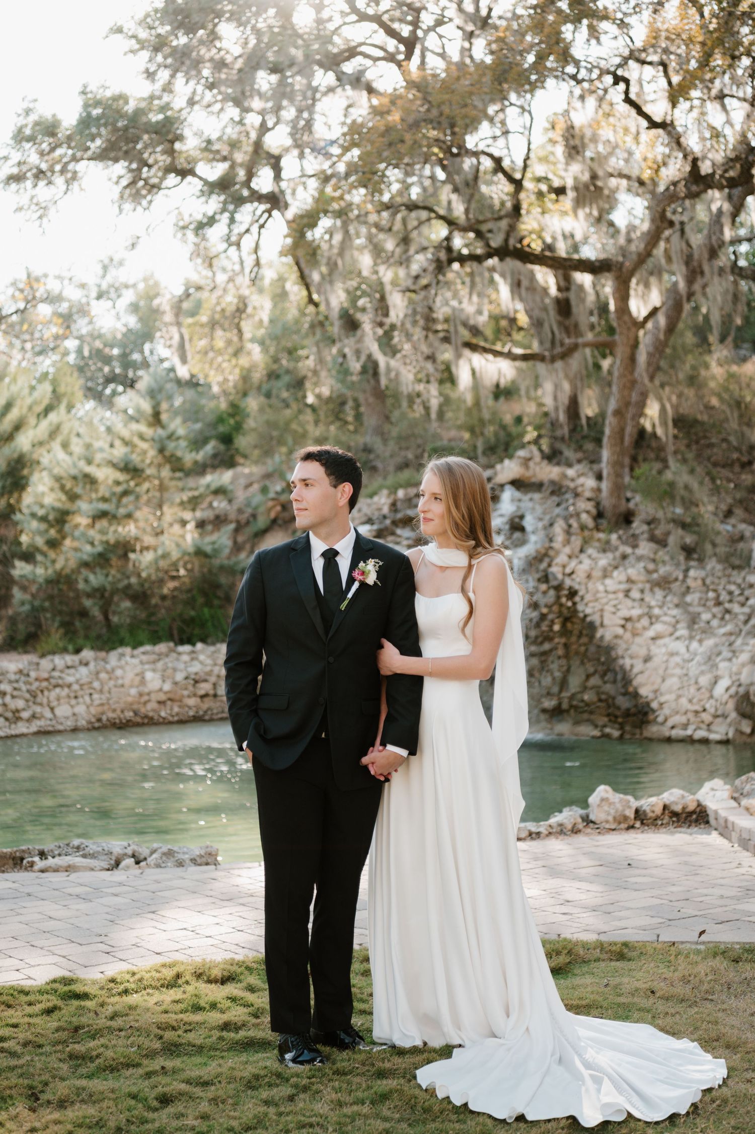 Newlyweds share a romantic moment by a stone wall and water feature.