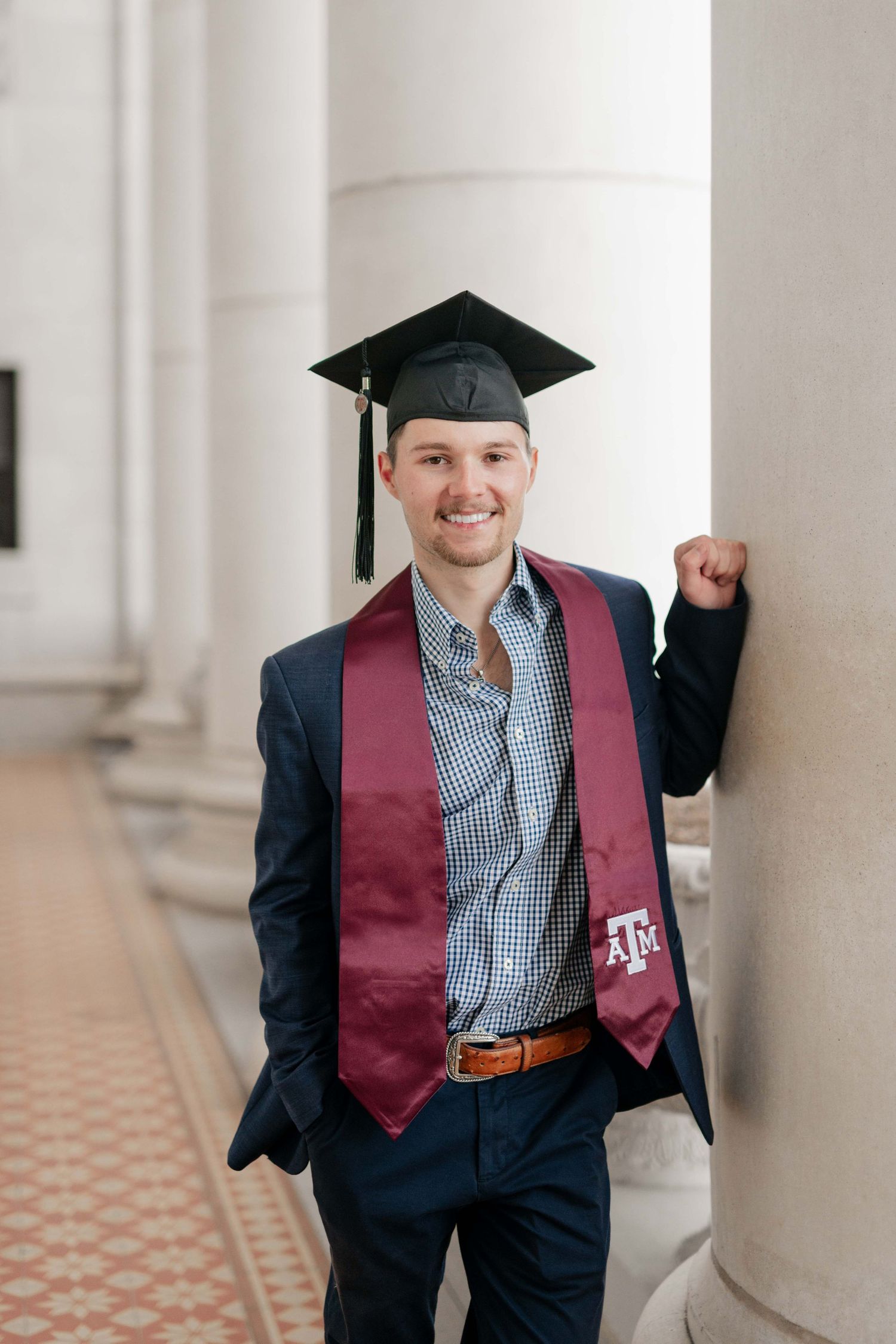 Graduate in Texas A&M regalia poses beside white columns.
