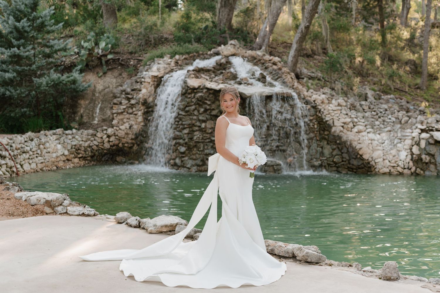 A couple poses near a turquoise mountain stream surrounded by rocky cliffs and evergreen trees in a scenic setting.