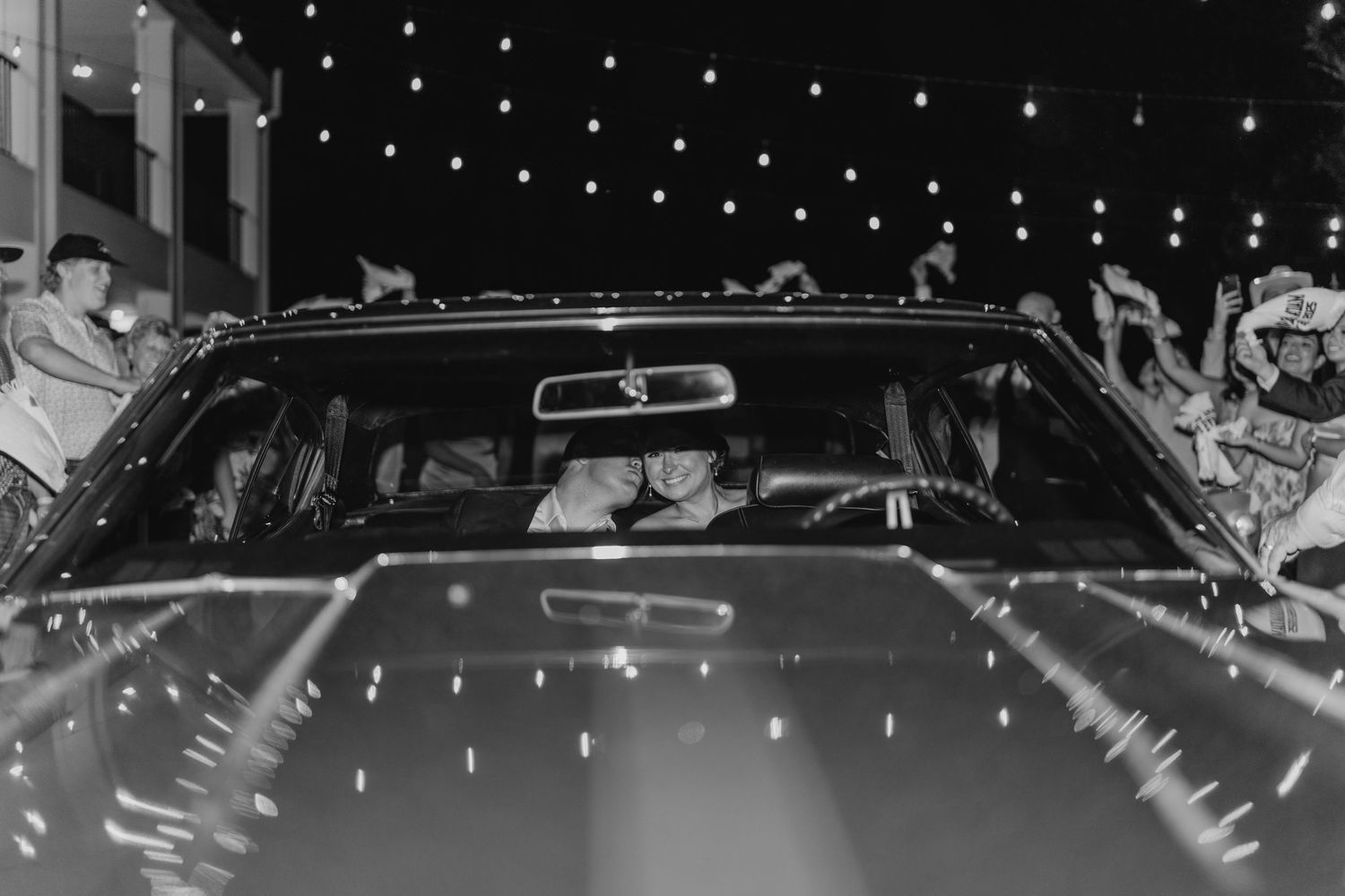 Car decorated with string lights and wedding decor during nighttime sendoff.