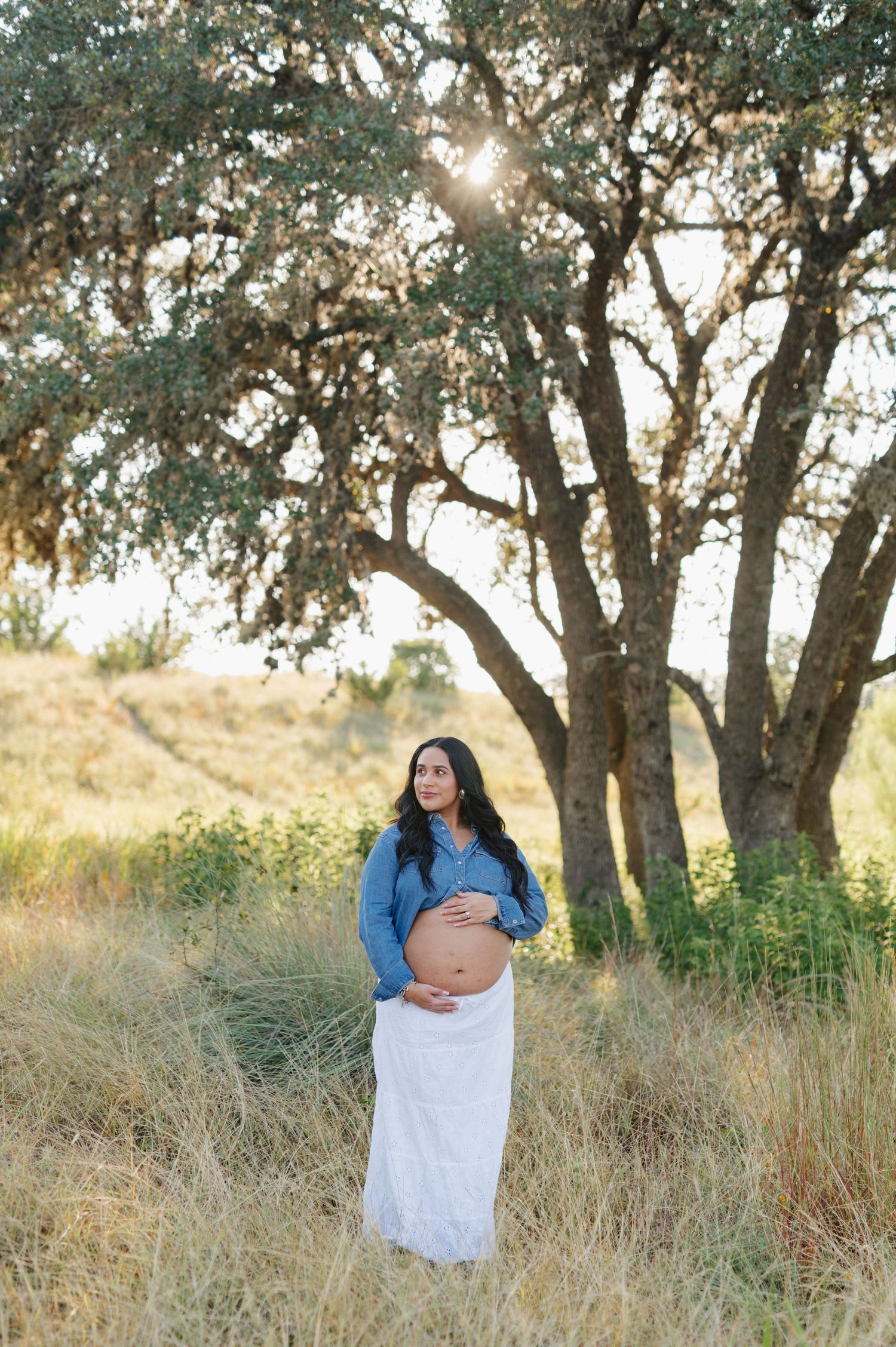 Beautiful maternity photography captures tender moments in a rustic outdoor setting with oak trees.