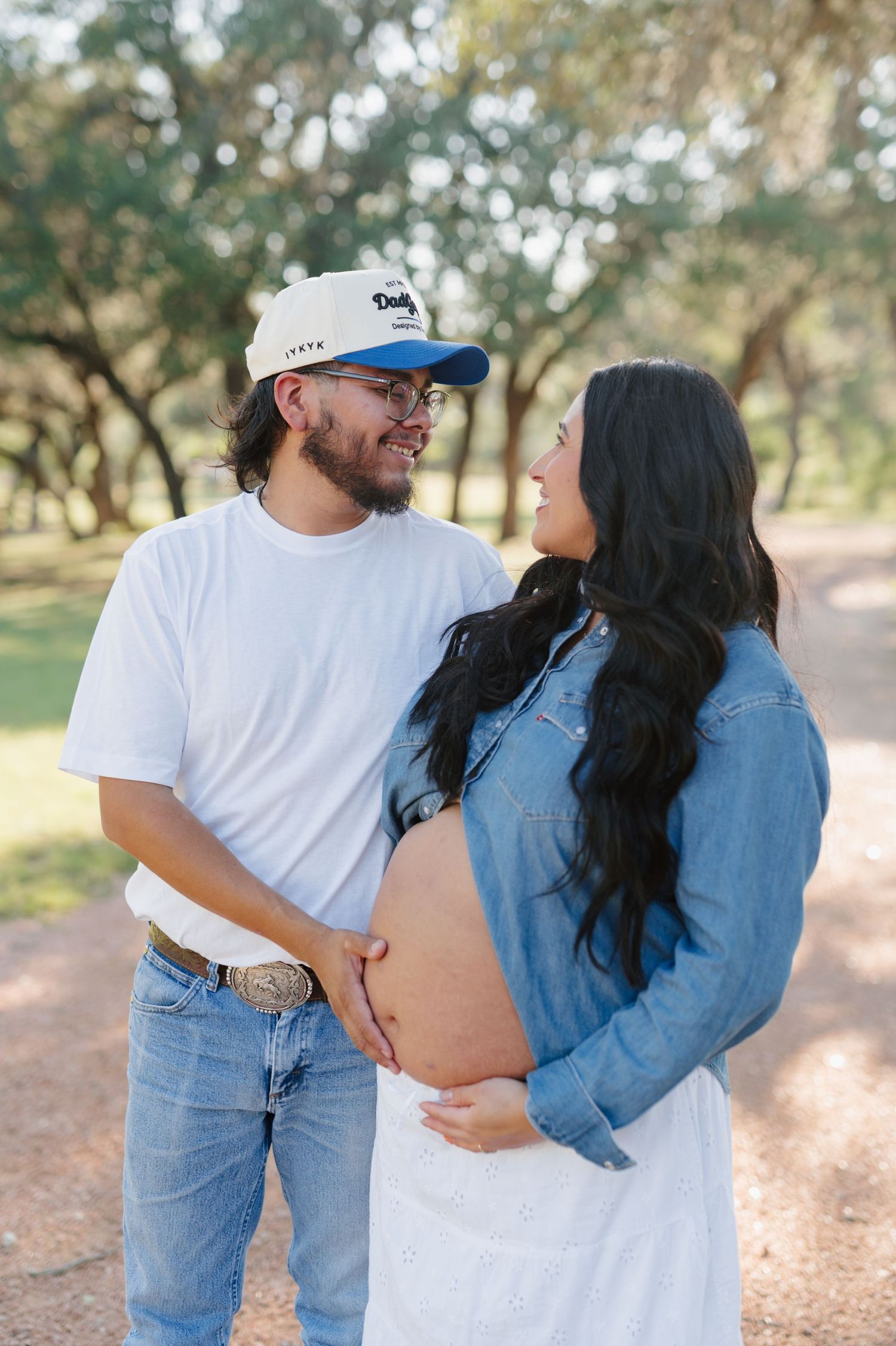 A couple in denim and white embraces outdoors, showing romantic affection in a natural setting.