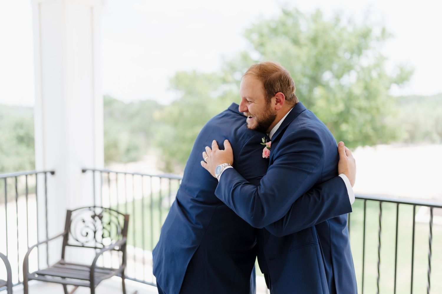 Wedding party gathers for emotional hugs on a white porch during outdoor celebration.