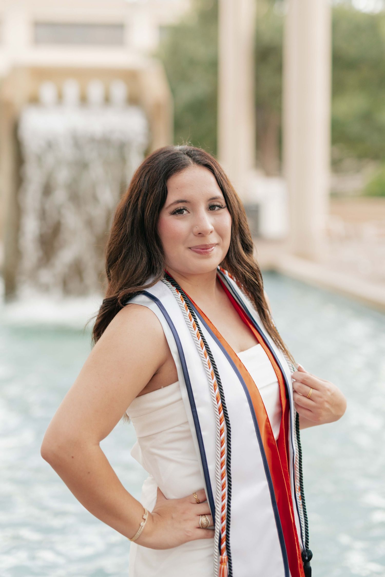 Graduate wearing ceremonial stole poses by water feature.