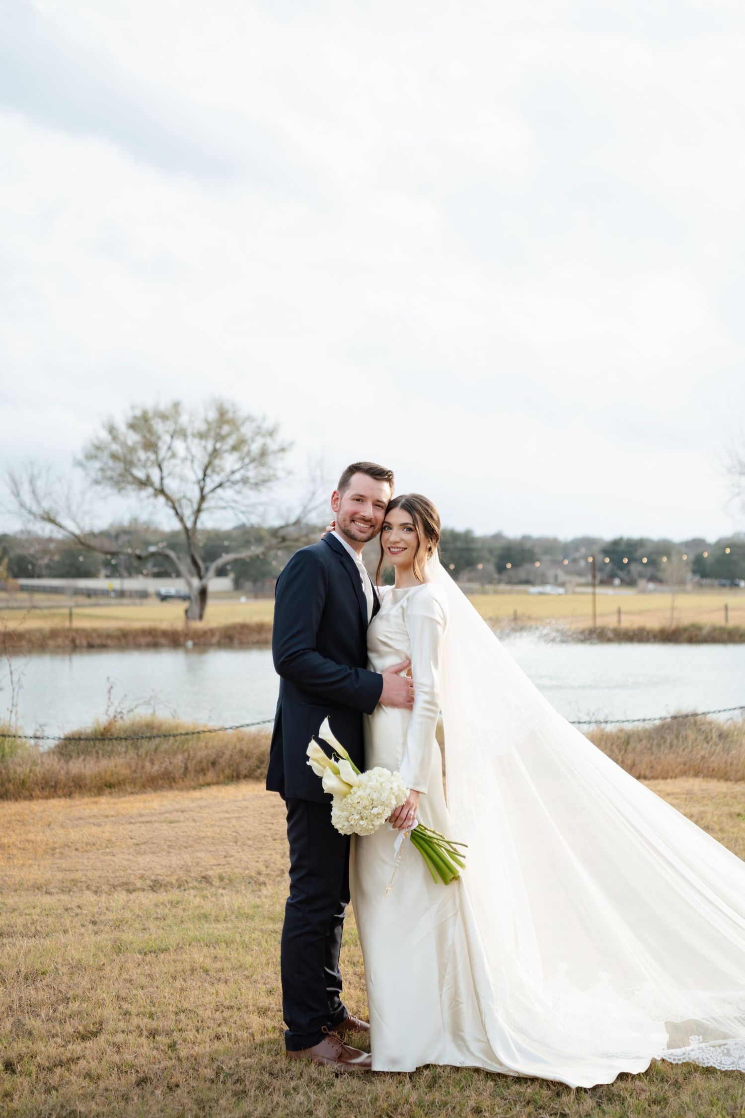 Newlyweds pose for romantic photos in an outdoor marsh setting with flowing white dress.