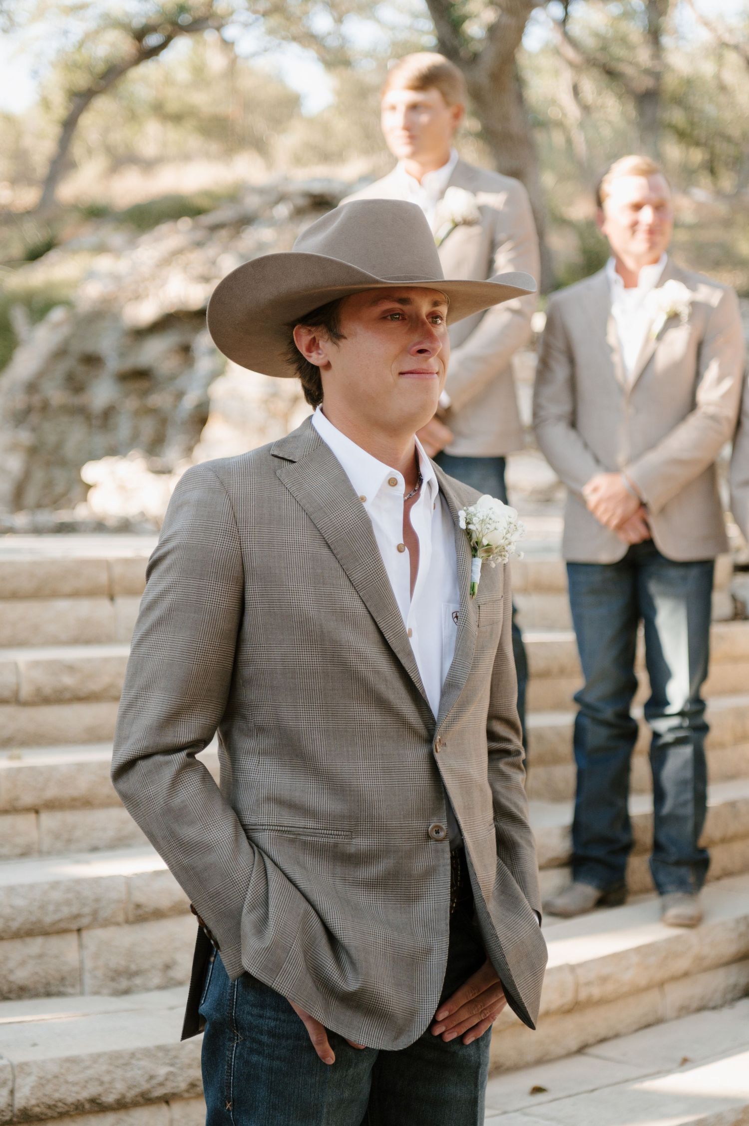 Groom in western attire and gray suit poses confidently outdoors.