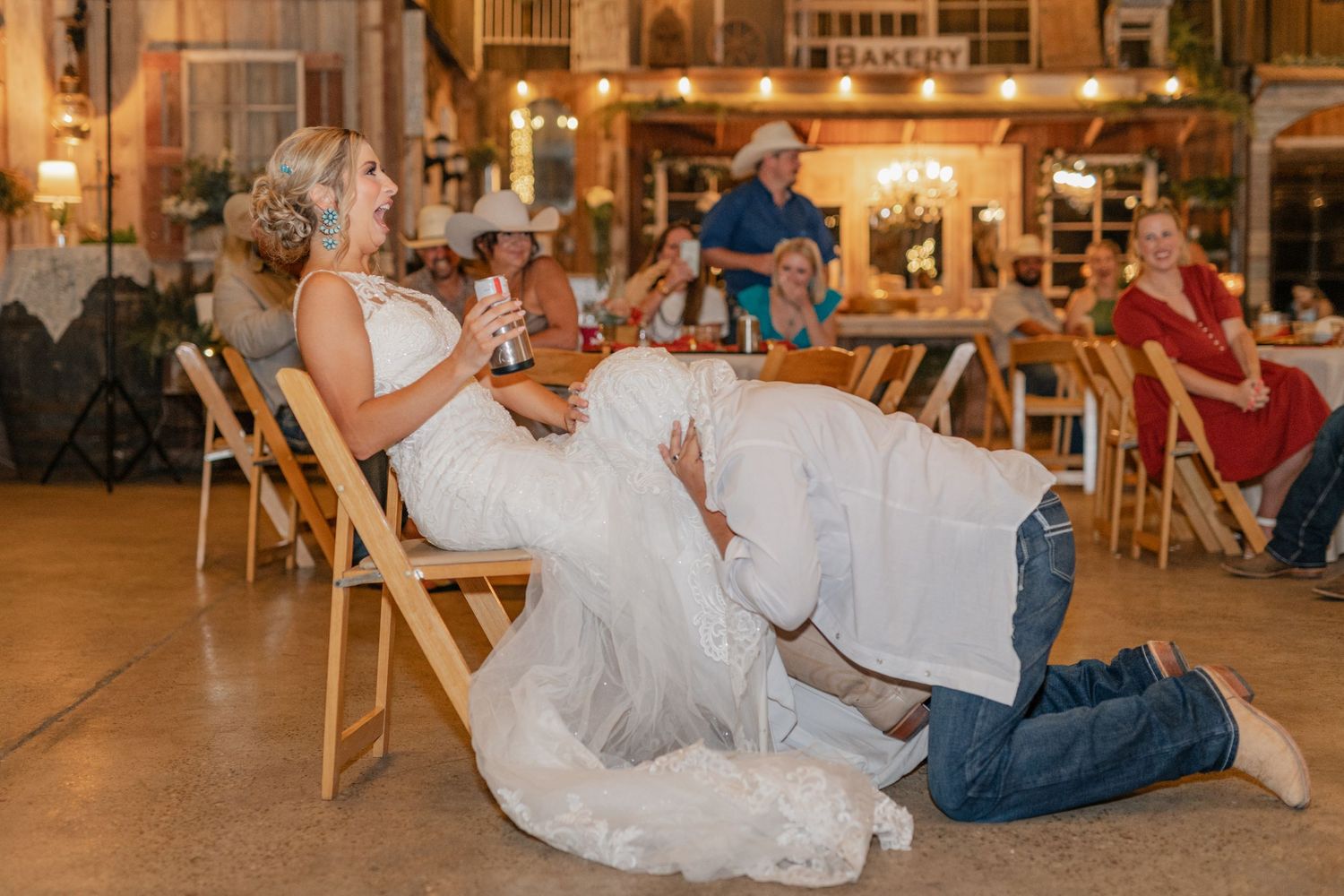 Fun wedding reception moment captured in rustic barn venue with wooden folding chairs.