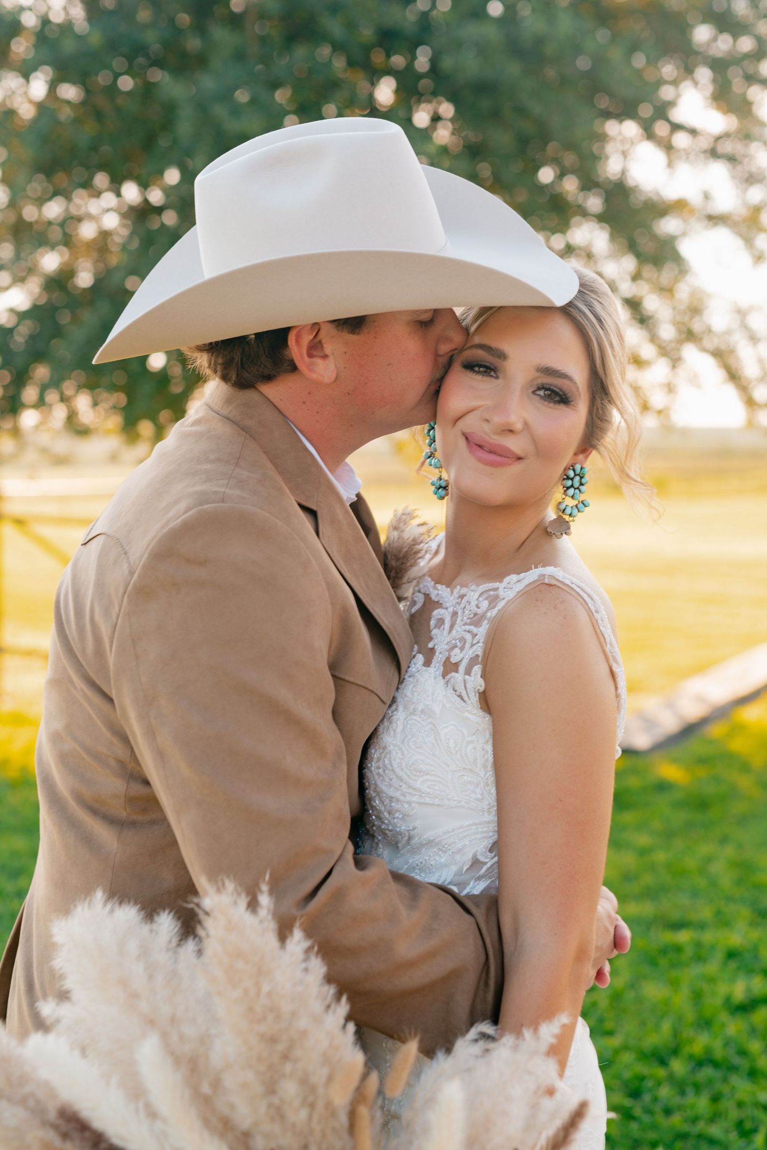 Intimate wedding moment captured in golden sunlight with rustic cowboy attire and lace dress.
